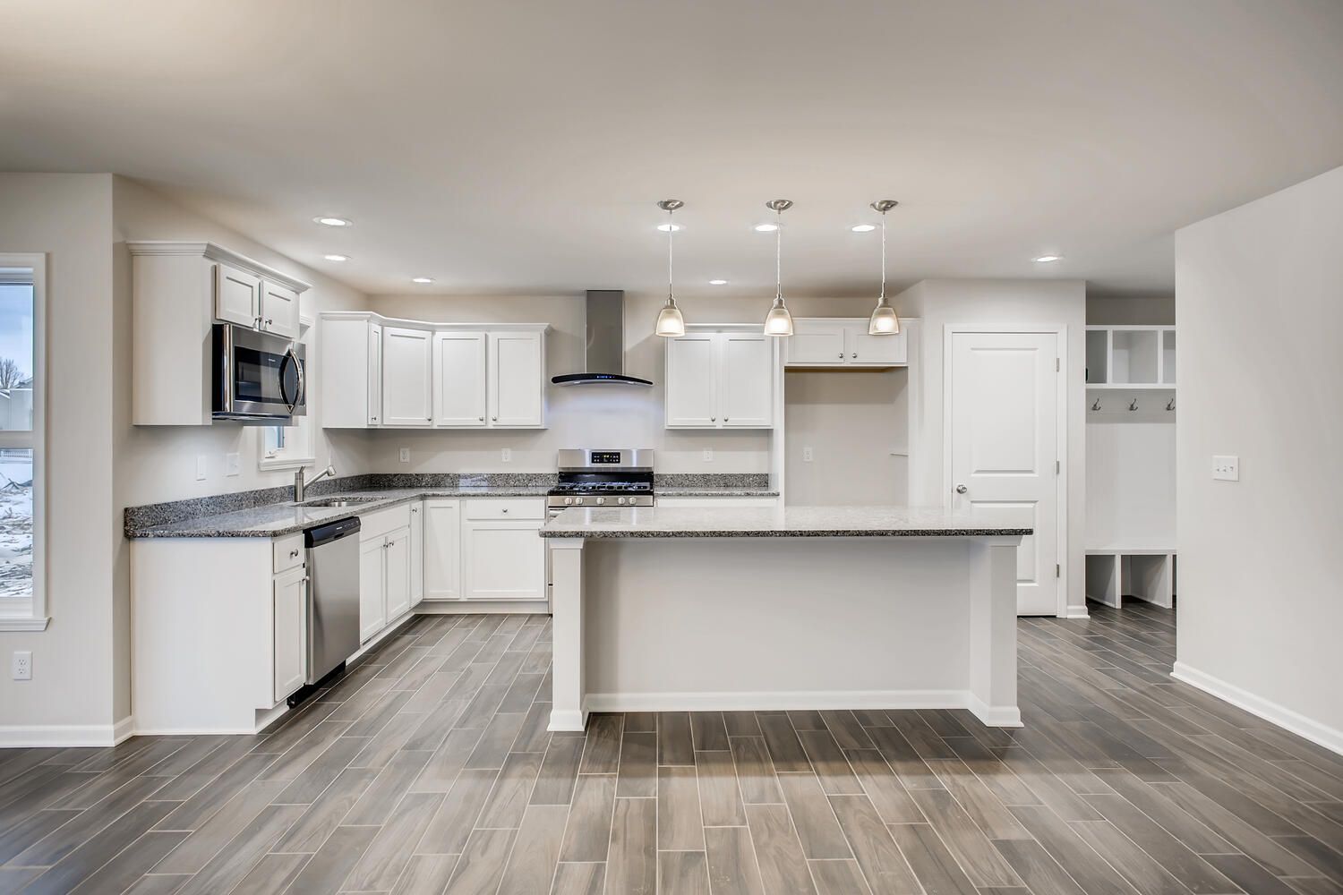 Bright, modern kitchen with white cabinets, stainless steel appliances, and island; wood-look flooring.