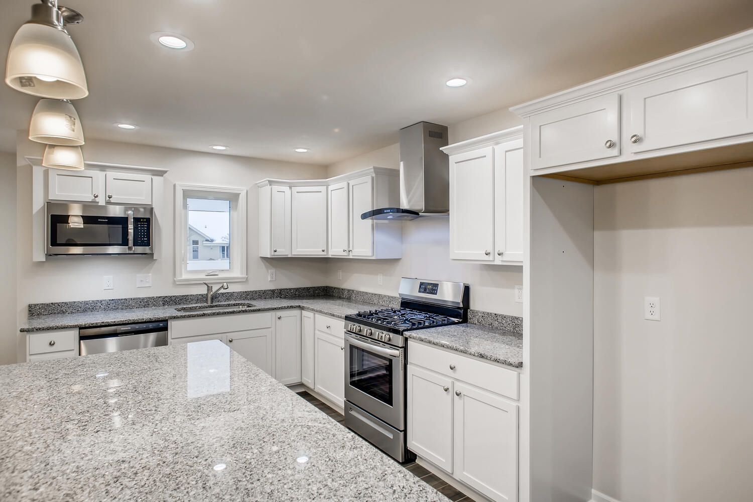 Bright kitchen with white cabinets, stainless steel appliances, and granite countertops.