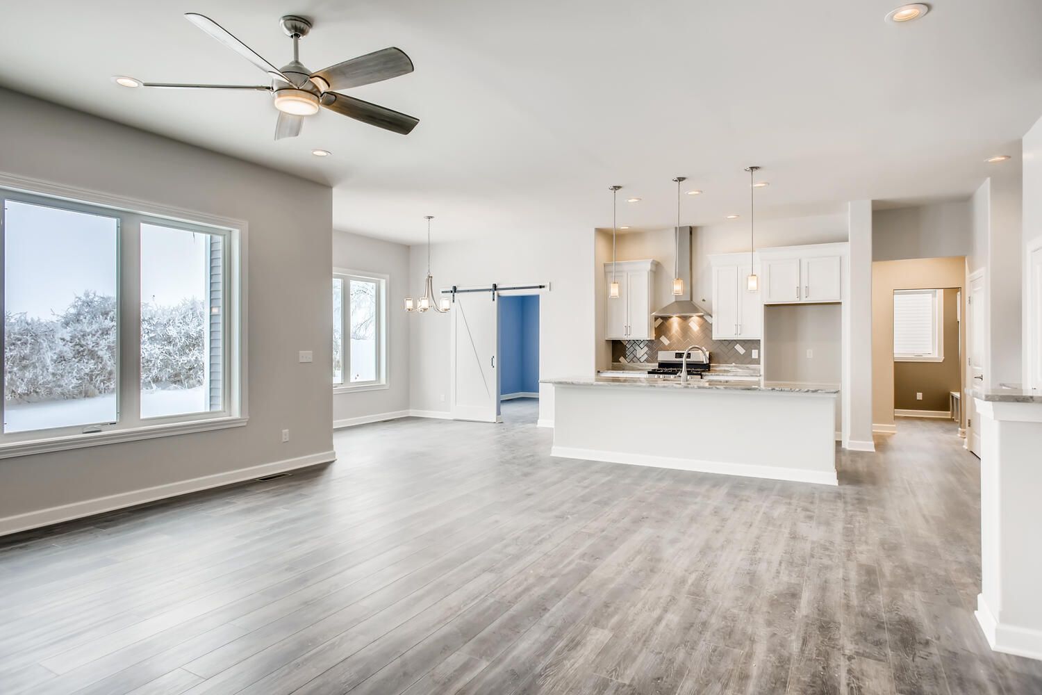 Spacious modern home interior with grey flooring, kitchen, and large windows overlooking a snowy landscape.