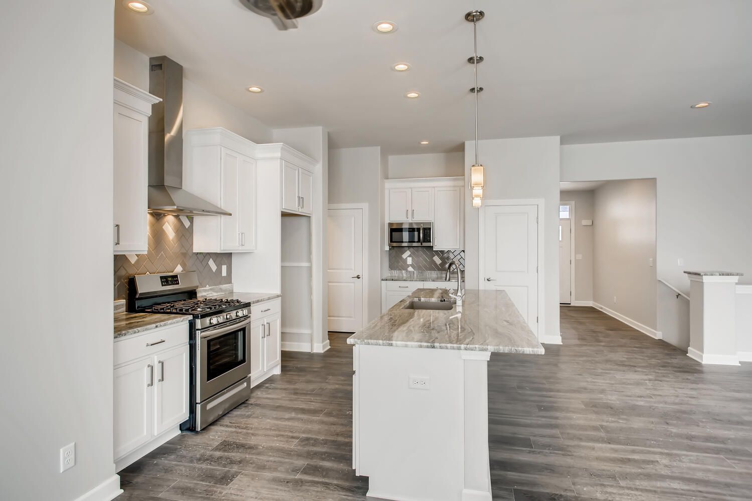 Modern white kitchen with island, stainless steel appliances, and gray flooring.