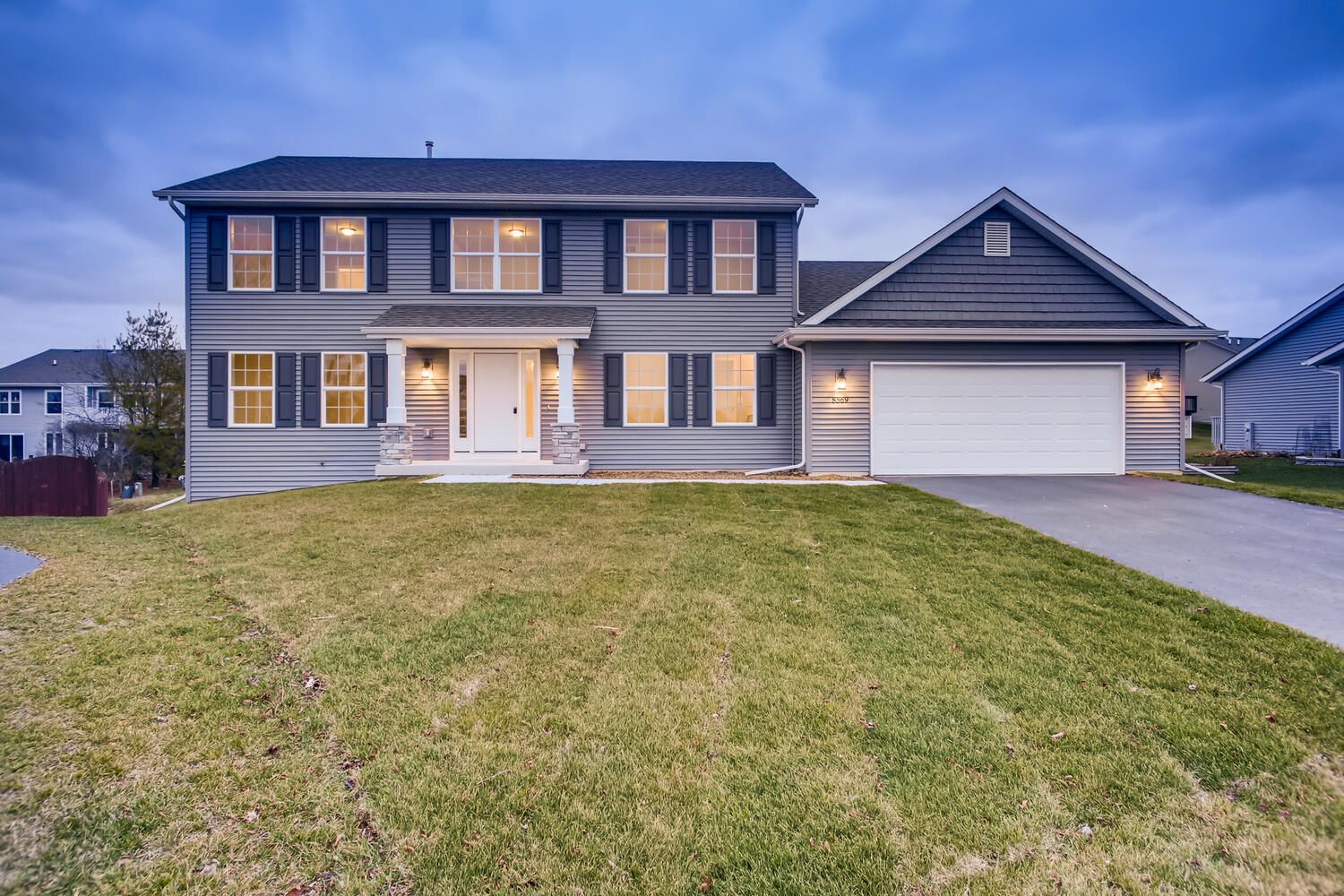 Two-story gray house with a driveway and garage, green lawn, blue sky in the background.