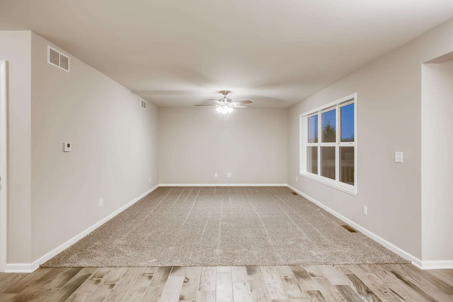 Empty room with beige walls, carpet, and a large window.