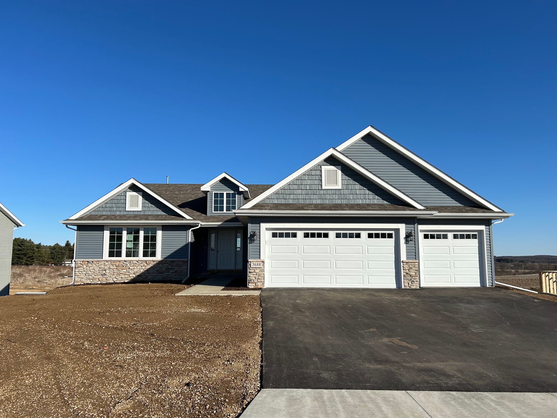 Blue house with white garage doors, stone accents, and a paved driveway under a blue sky.