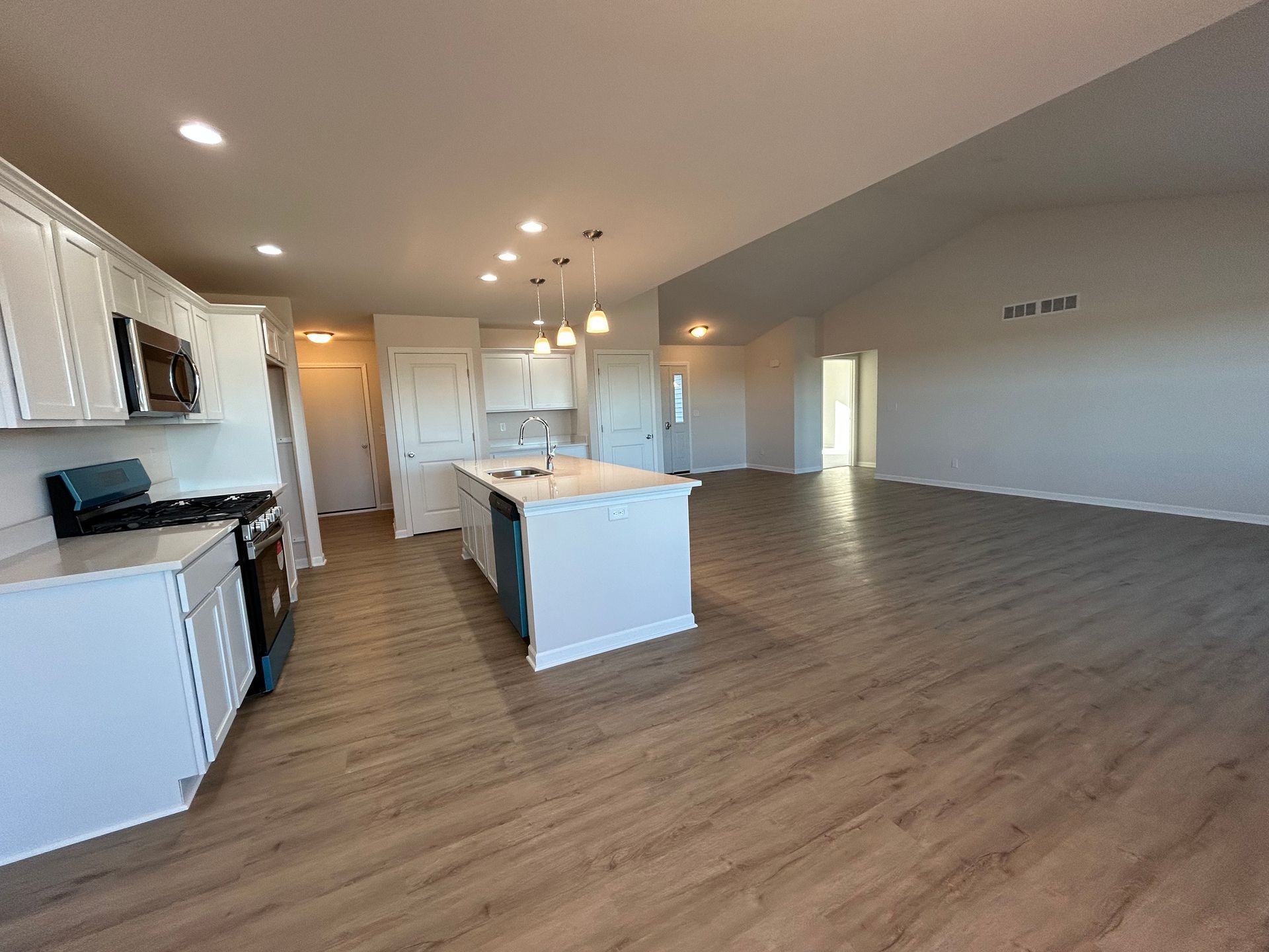 Modern kitchen with white cabinets, island, and wood-look flooring, open to a spacious living area.