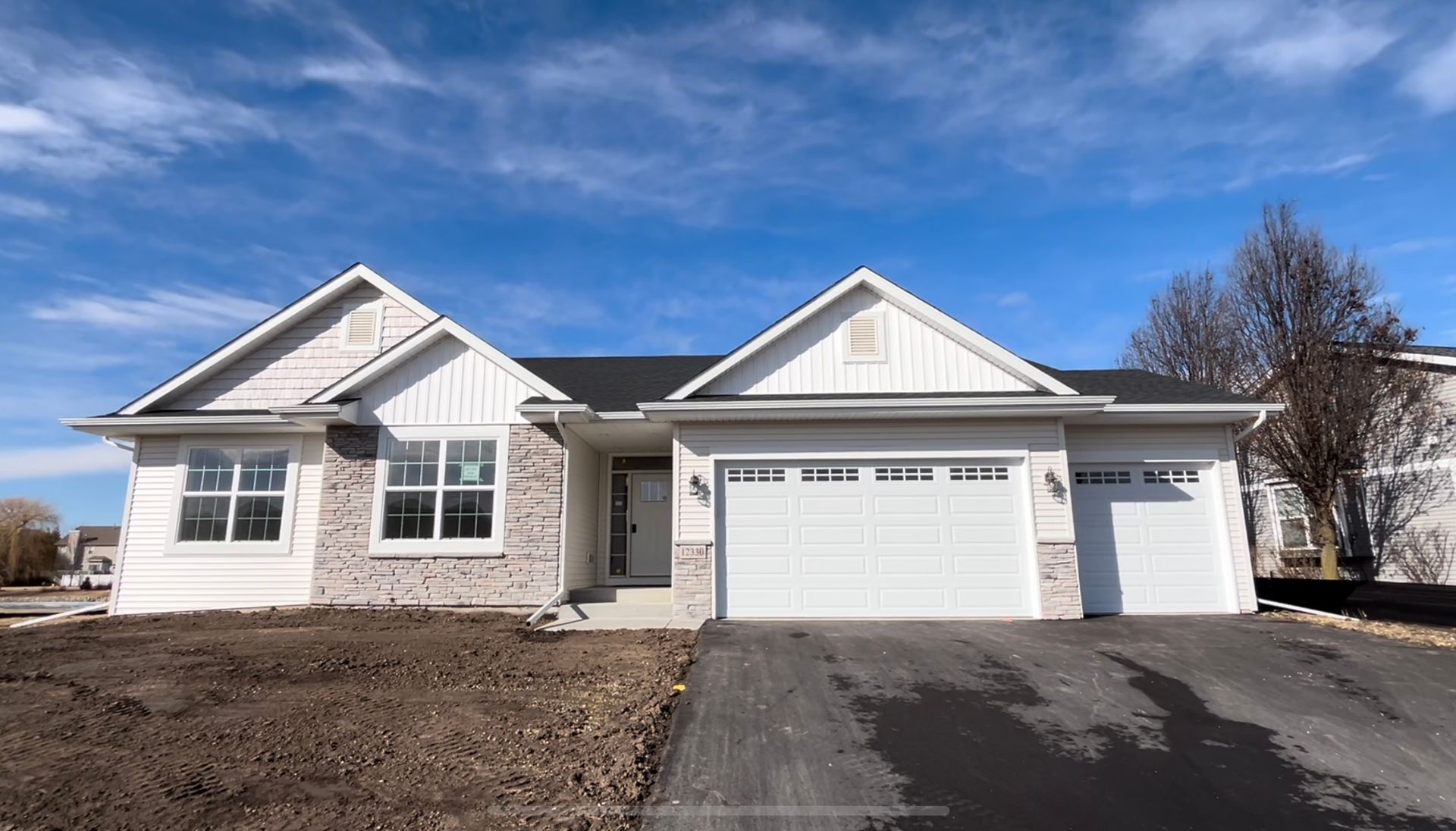 Single-story white house with two-car garage, brick accents, and asphalt driveway against a blue sky.