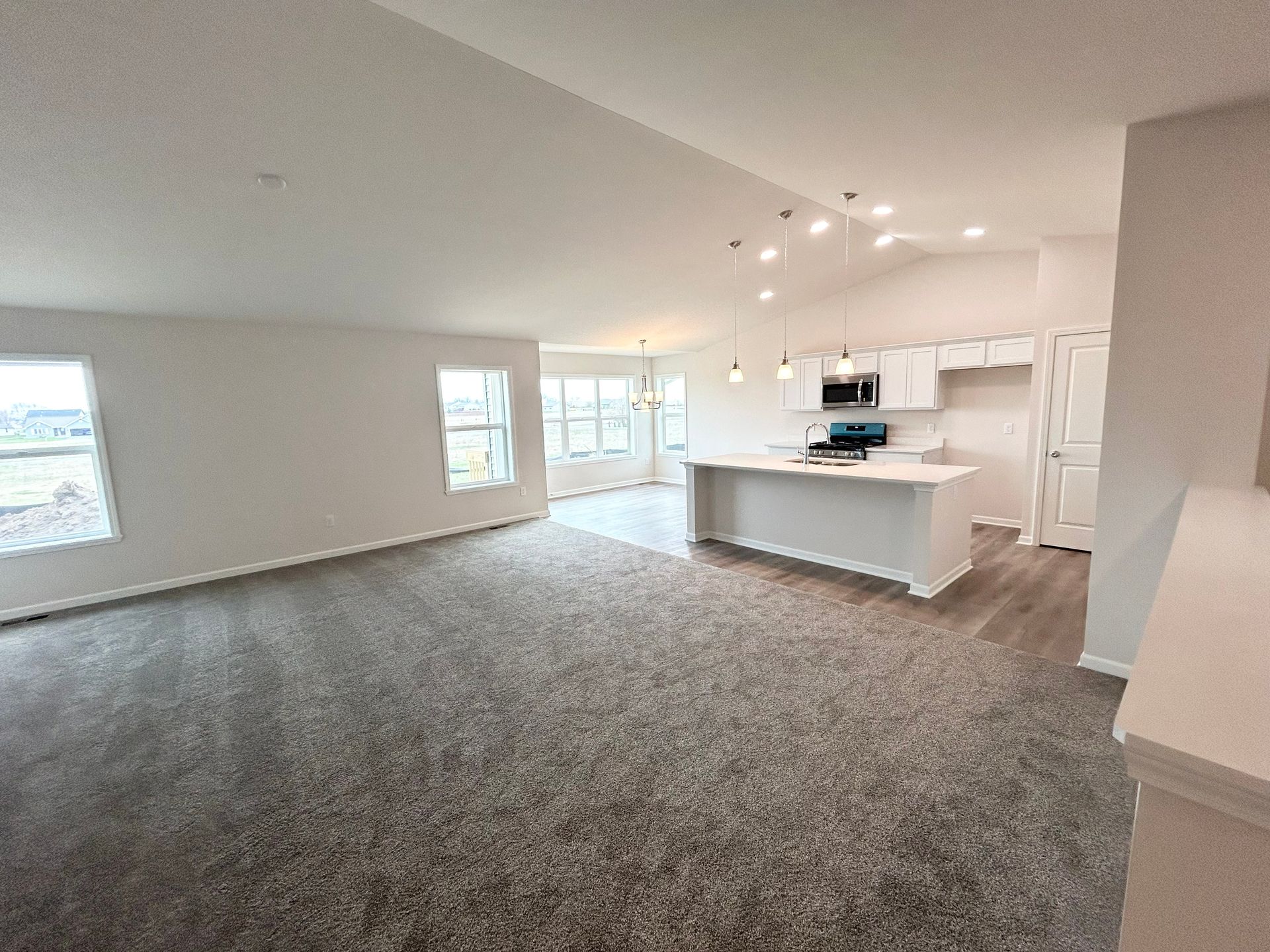Open-concept living space: white walls, kitchen island, carpet, and light fixtures.