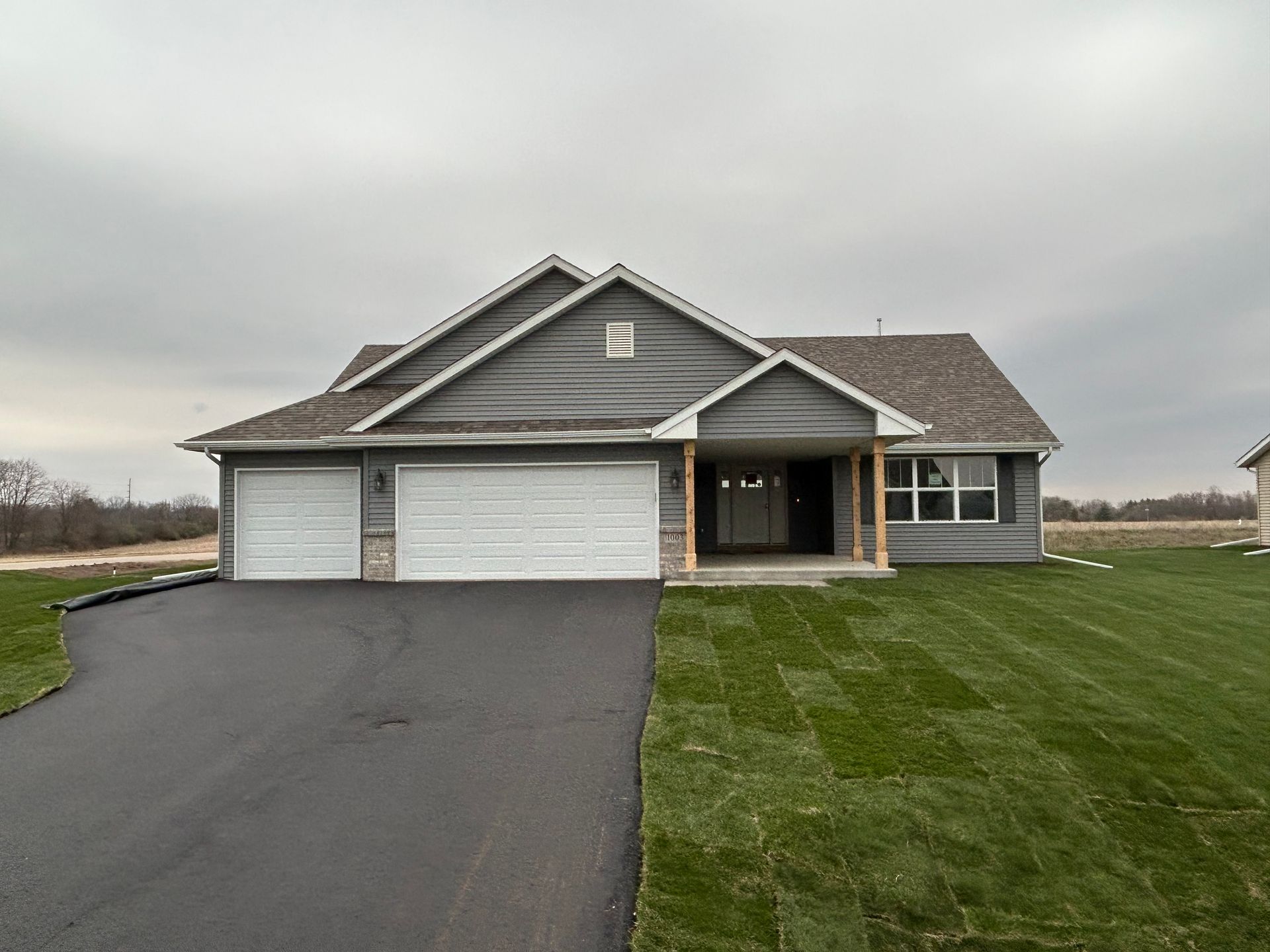 Gray house with a two-car garage, new grass, and a dark asphalt driveway under an overcast sky.
