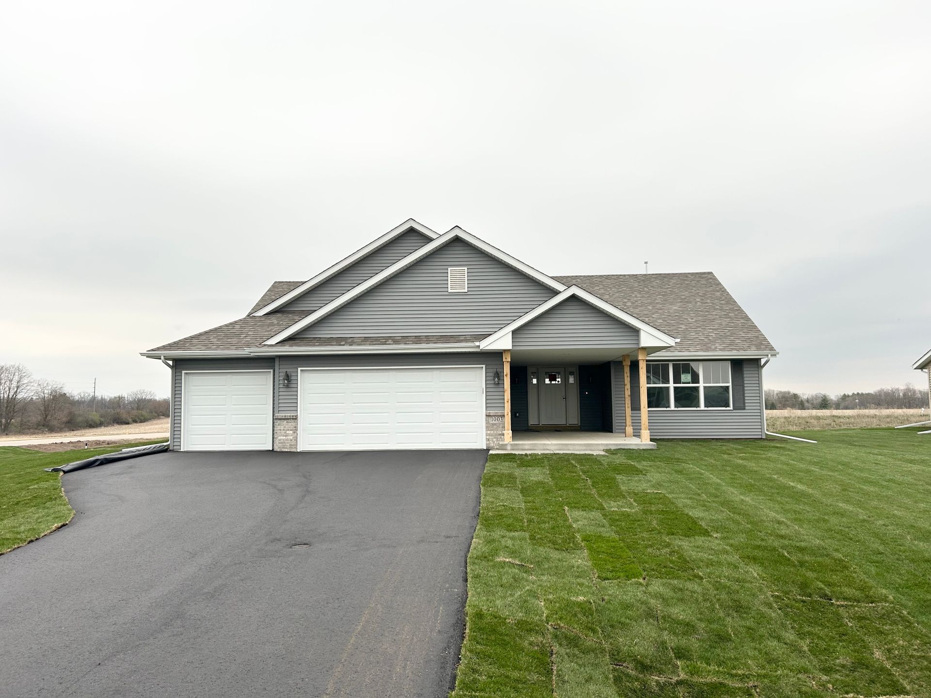 Gray house with attached garage, black driveway, green grass under a cloudy sky.