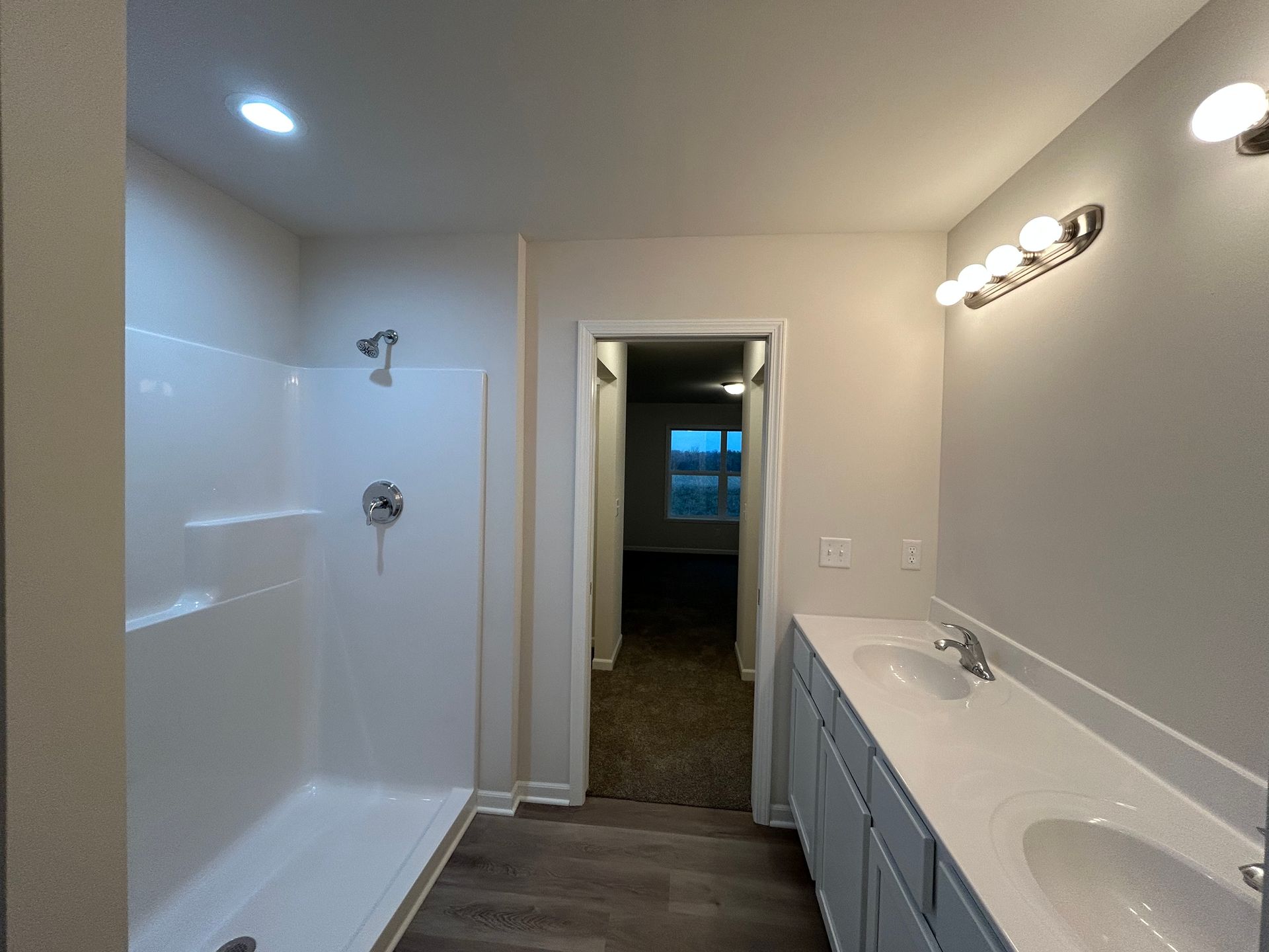 Bathroom with shower on the left, double sink vanity on the right, and doorway to a bedroom in the center.