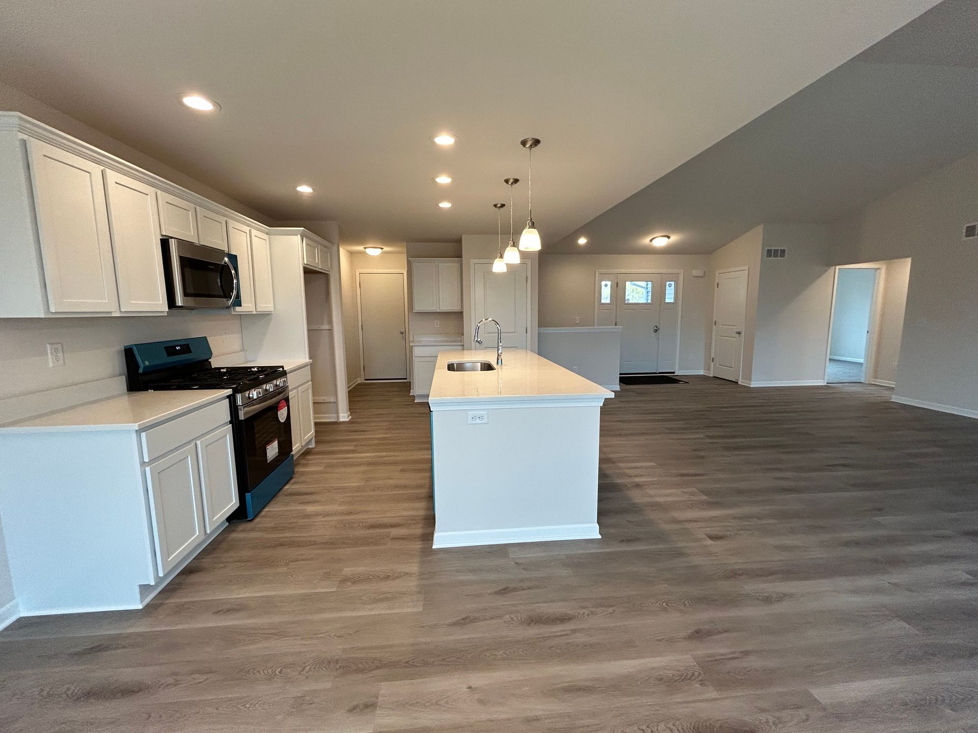 Bright, modern kitchen with white cabinets, island, and appliances; open to a living area with wood flooring.