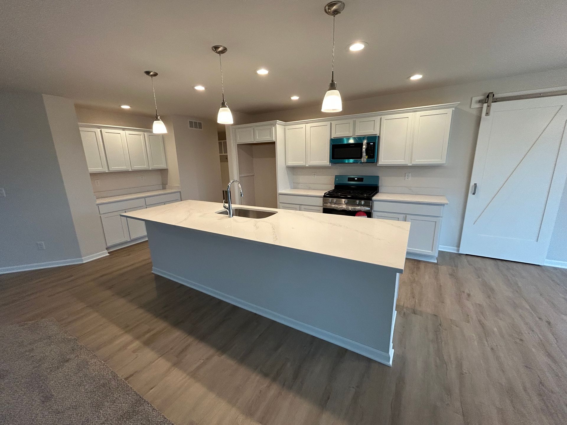 Modern kitchen with white cabinets, island, and appliances; wood flooring.