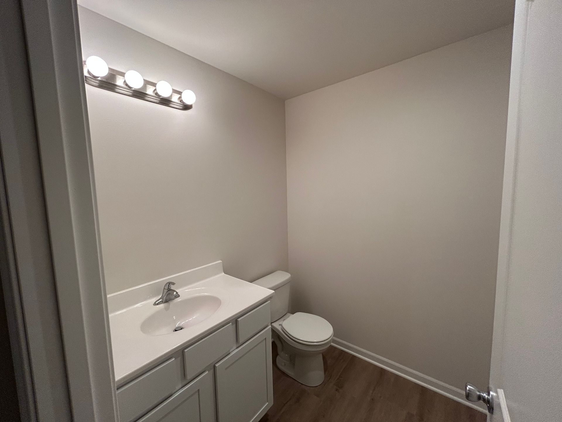 Bathroom with white vanity, toilet, light fixture, and light gray walls.