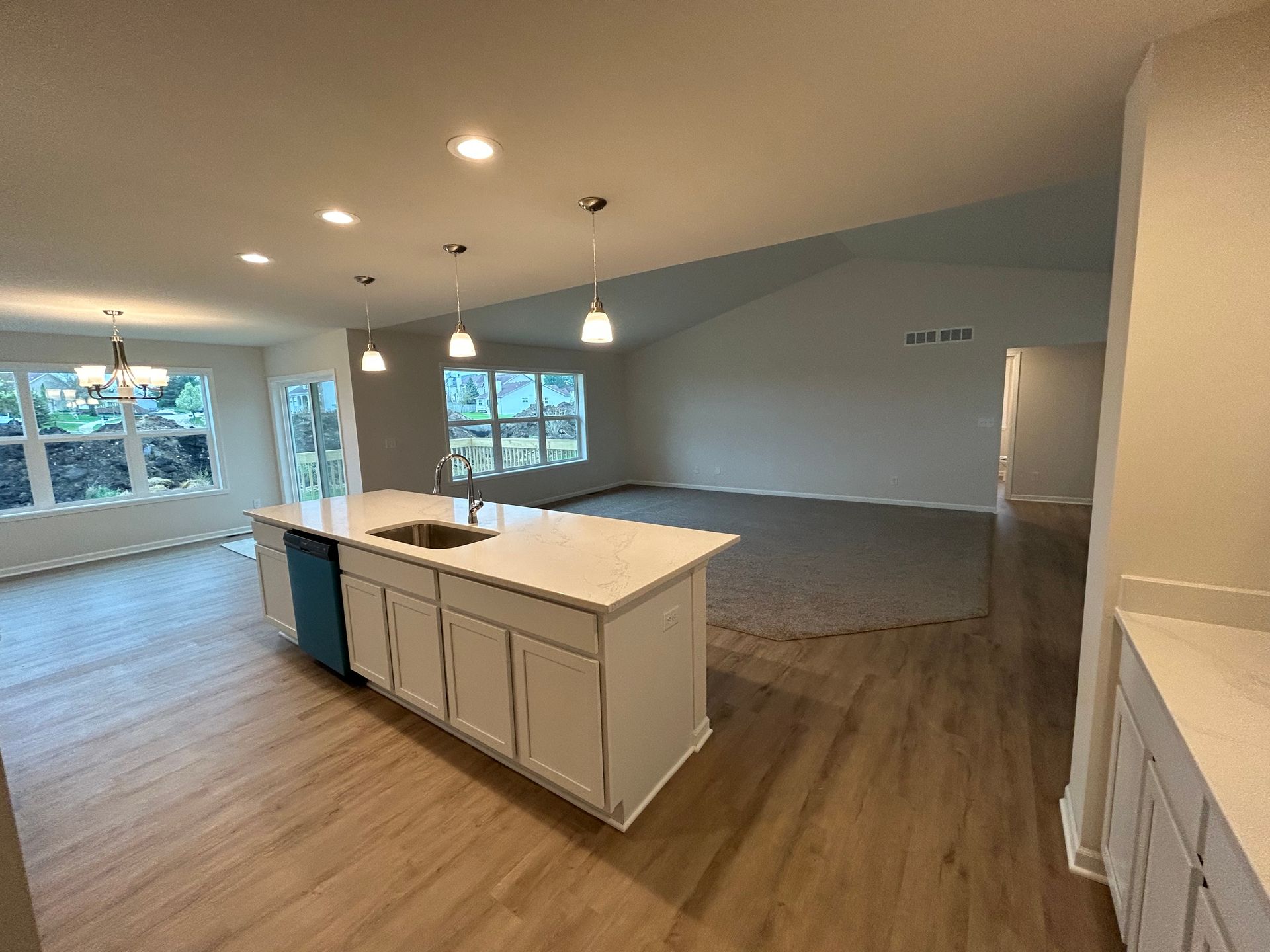 Spacious open-plan kitchen with white cabinets and island, light wood floors, and windows.