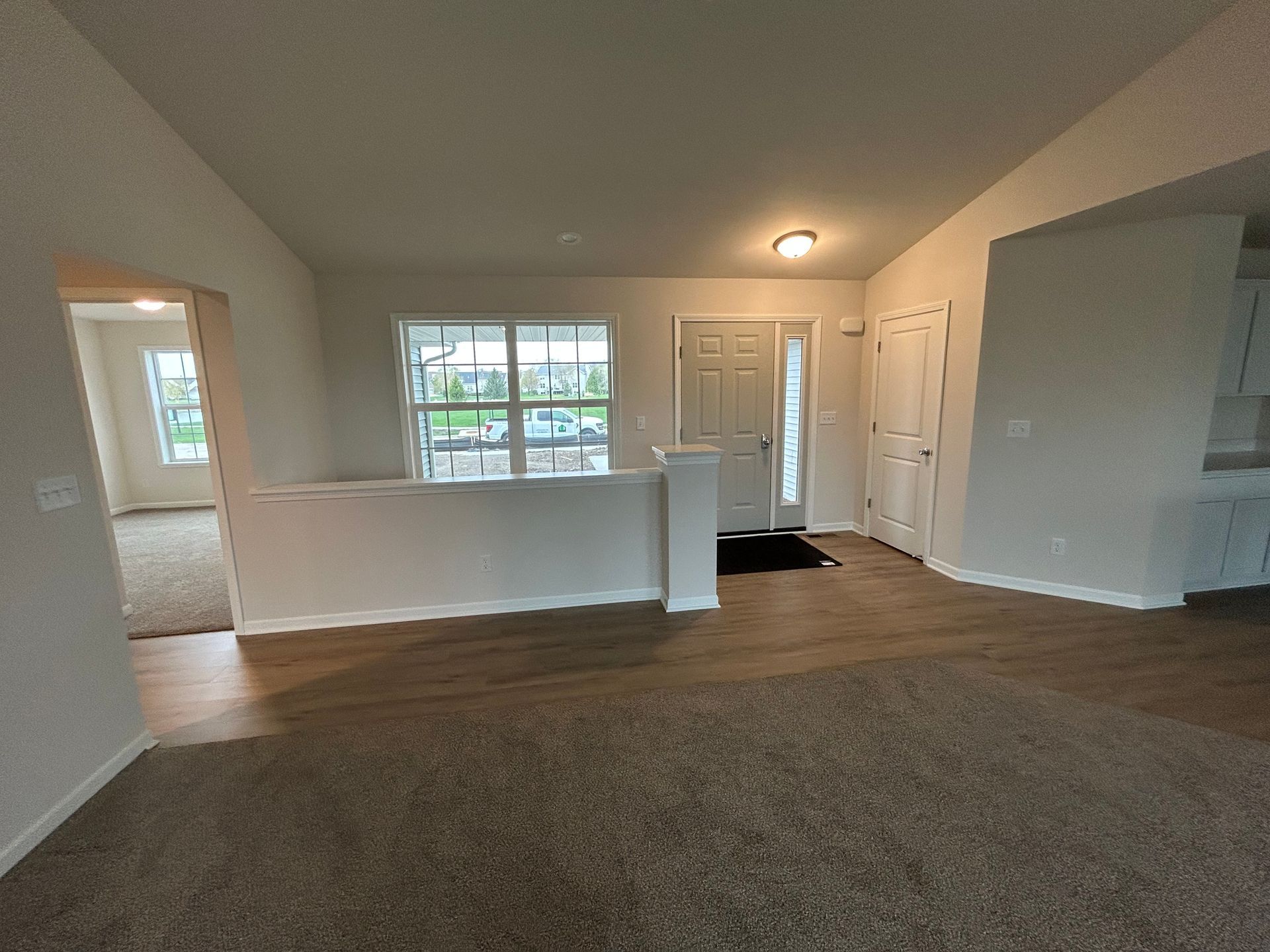 Interior view of a house with a light-filled living area, front door, and view to another room.