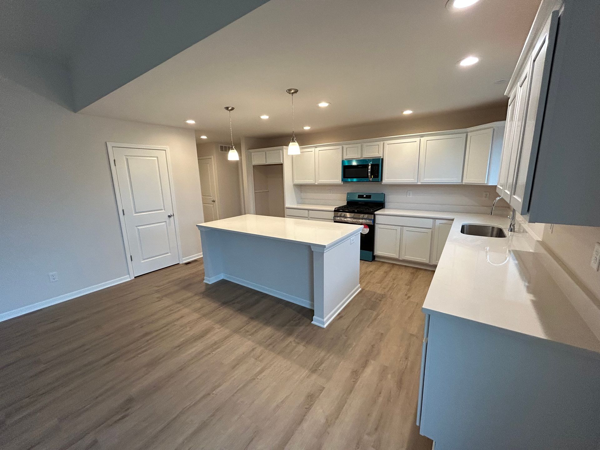 Modern kitchen with white cabinets, island, and appliances; gray wood-look flooring.