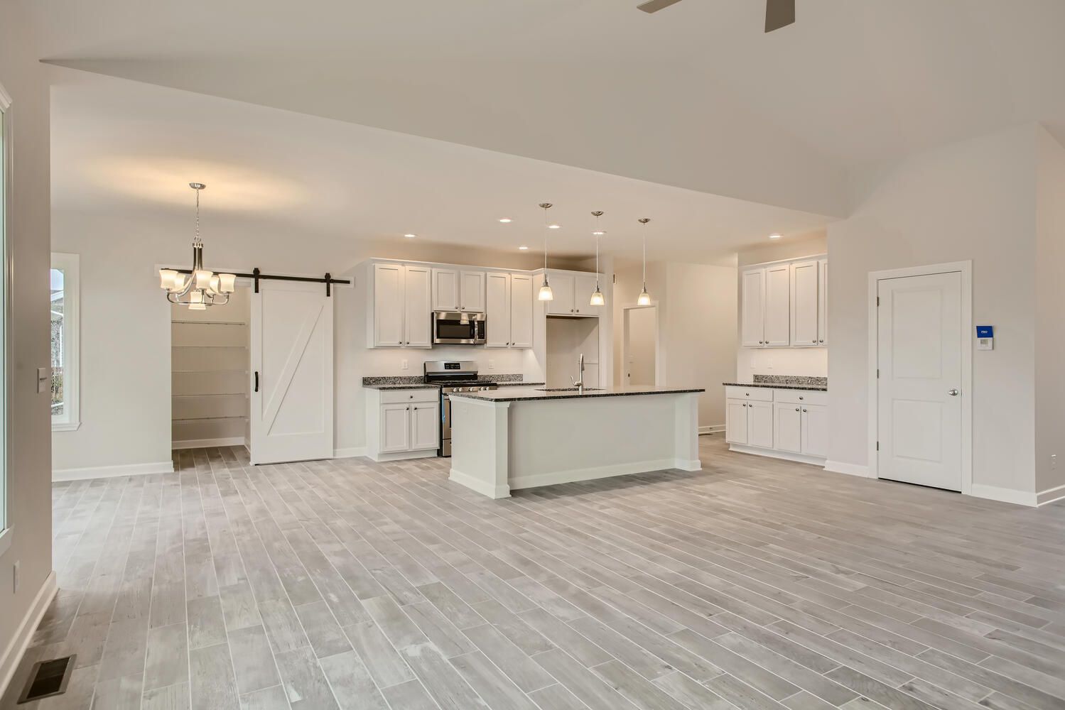 Open-concept kitchen with white cabinets, black island, gray floors. Barn door, pendant lights, and door.