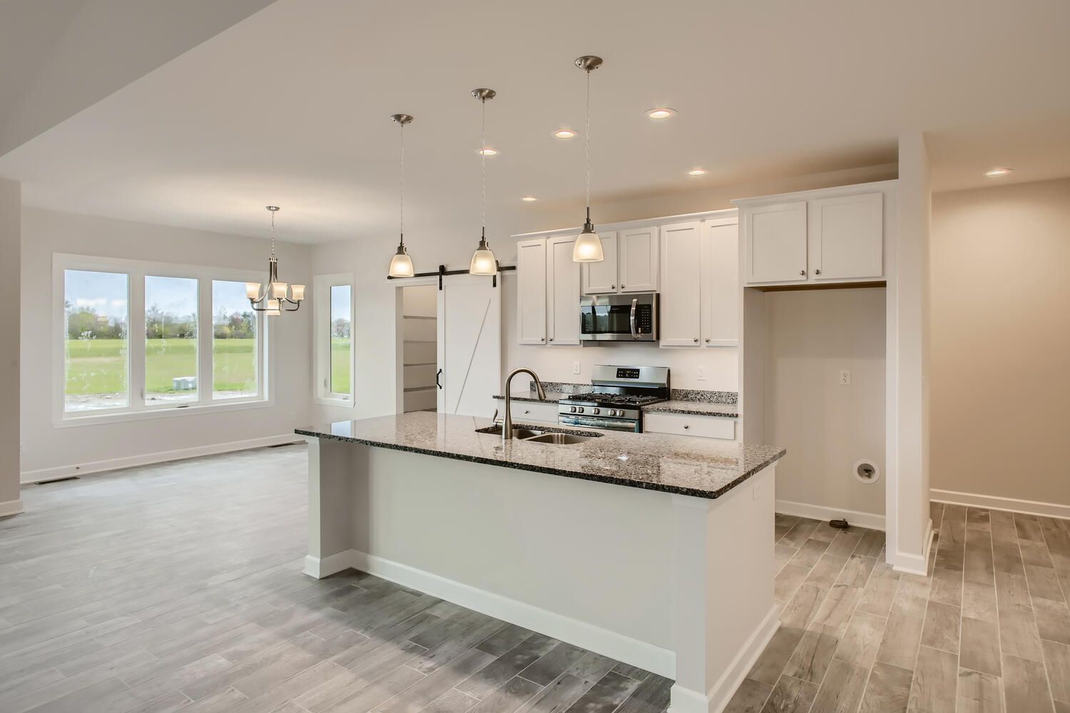 Open-concept kitchen with white cabinets, island, and gray wood-look floors.