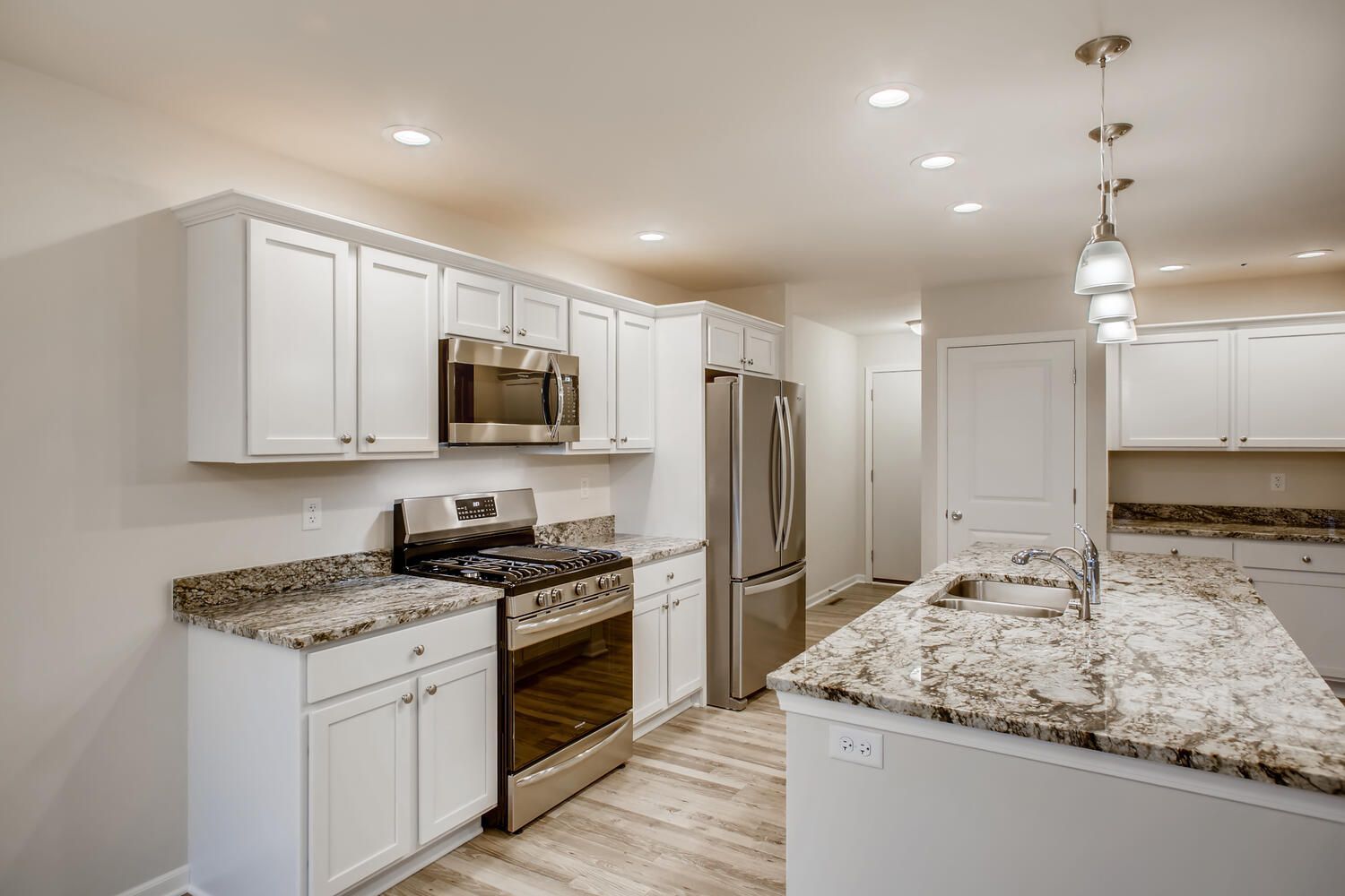 White kitchen with stainless steel appliances, granite countertops, and island.