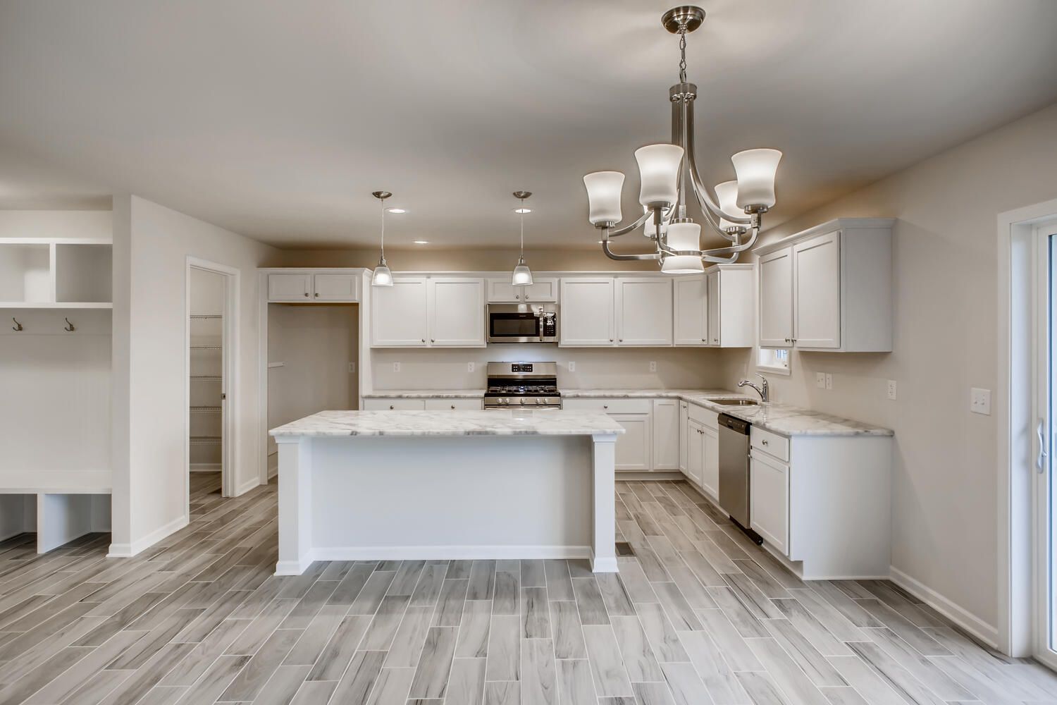 Modern white kitchen with island, stainless steel appliances, light wood flooring, and a chandelier.