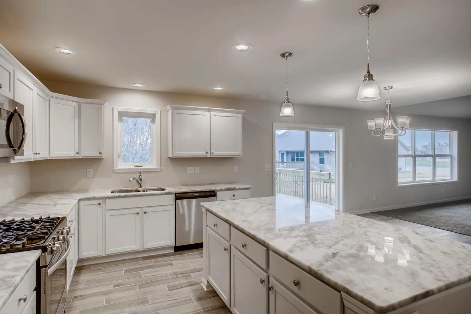 Bright, white kitchen with marble countertops, stainless steel appliances, and island.