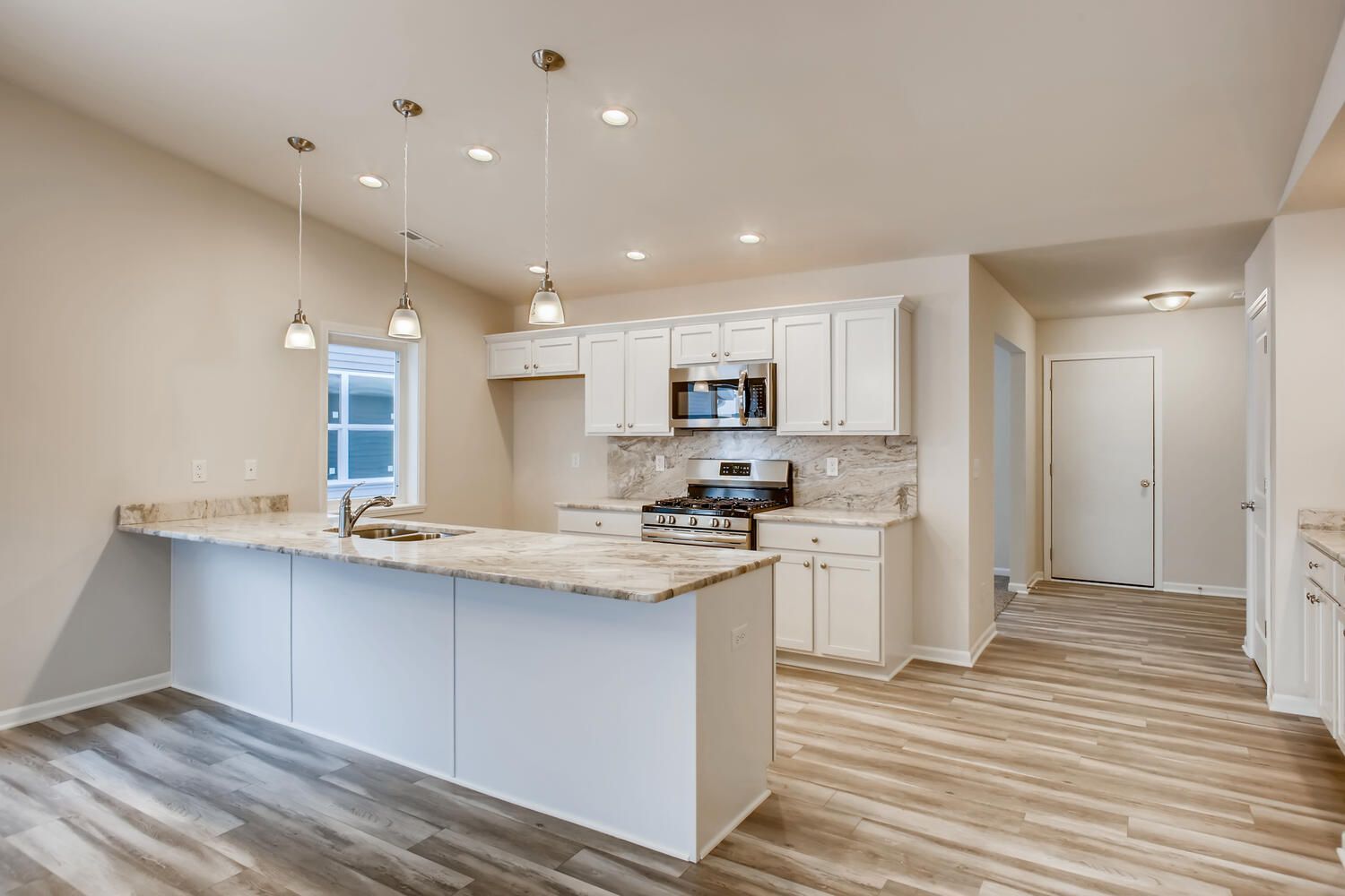 Bright, white kitchen with island and stainless steel appliances. Light wood floors.