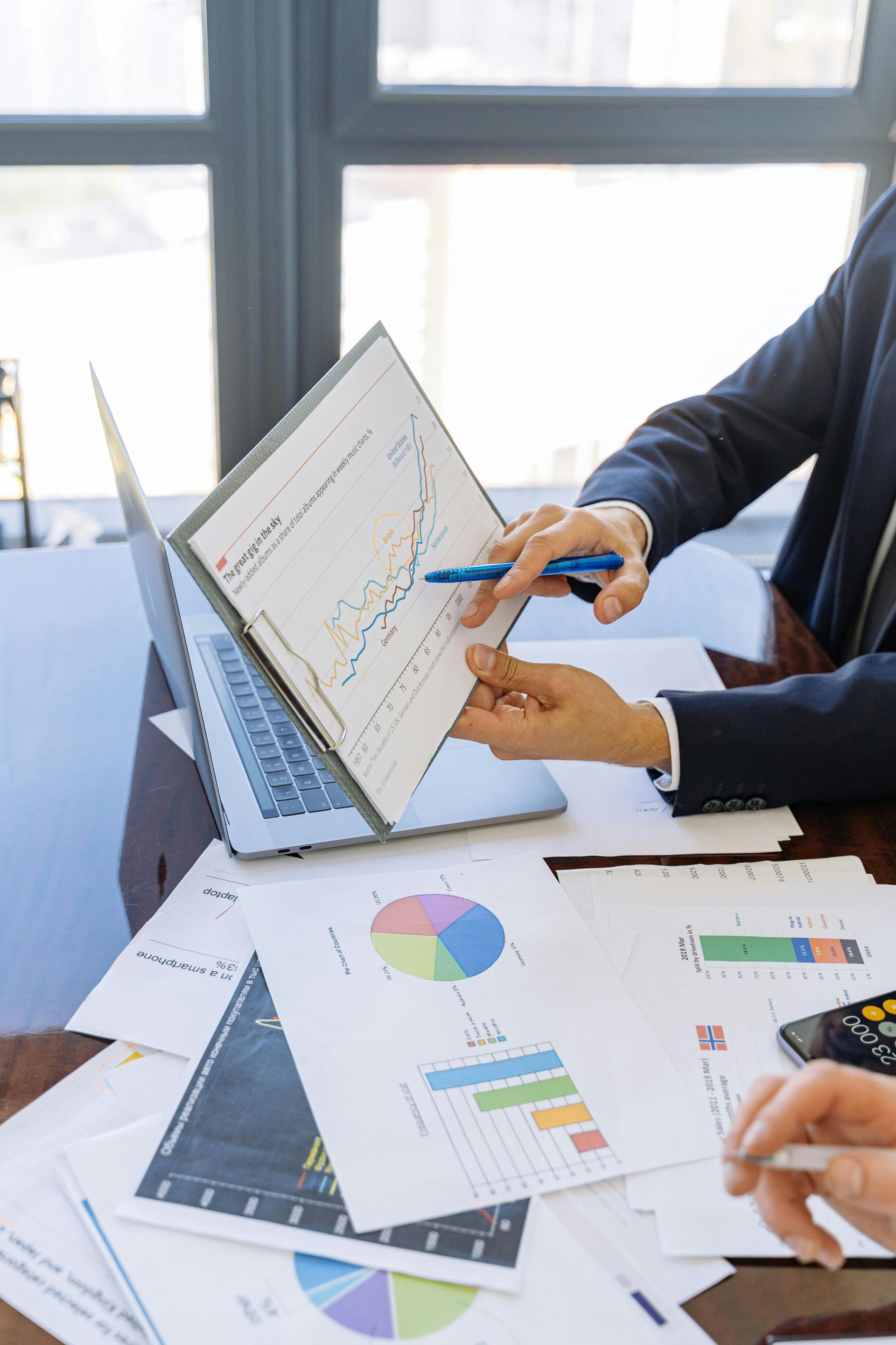 Business people reviewing charts, pointing at graphs, with a laptop, indoors, at a table.