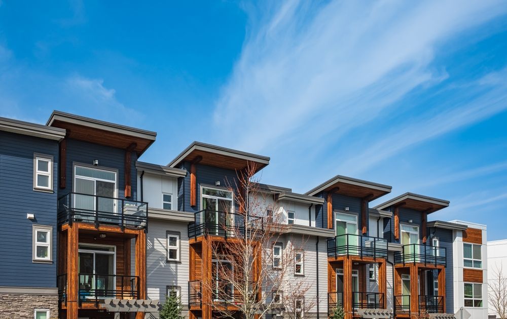 Modern townhouses with balconies, blue and grey exteriors, under a blue sky.