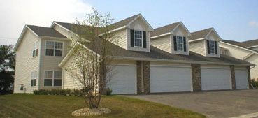 Row of townhouses with white siding, dark roof, and three garage doors.