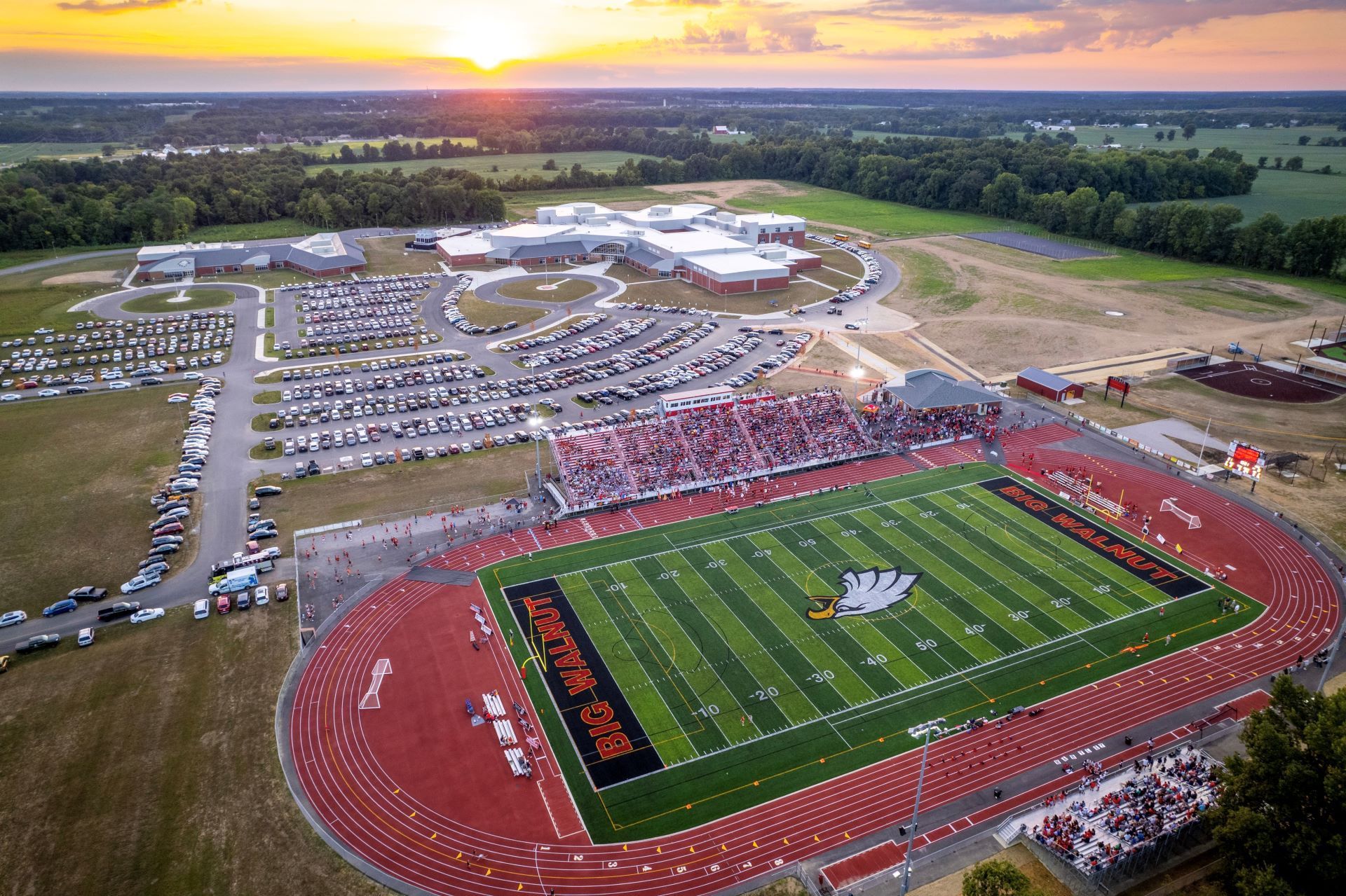 An aerial view of the Big Walnut football stadium with a sunset in the background.