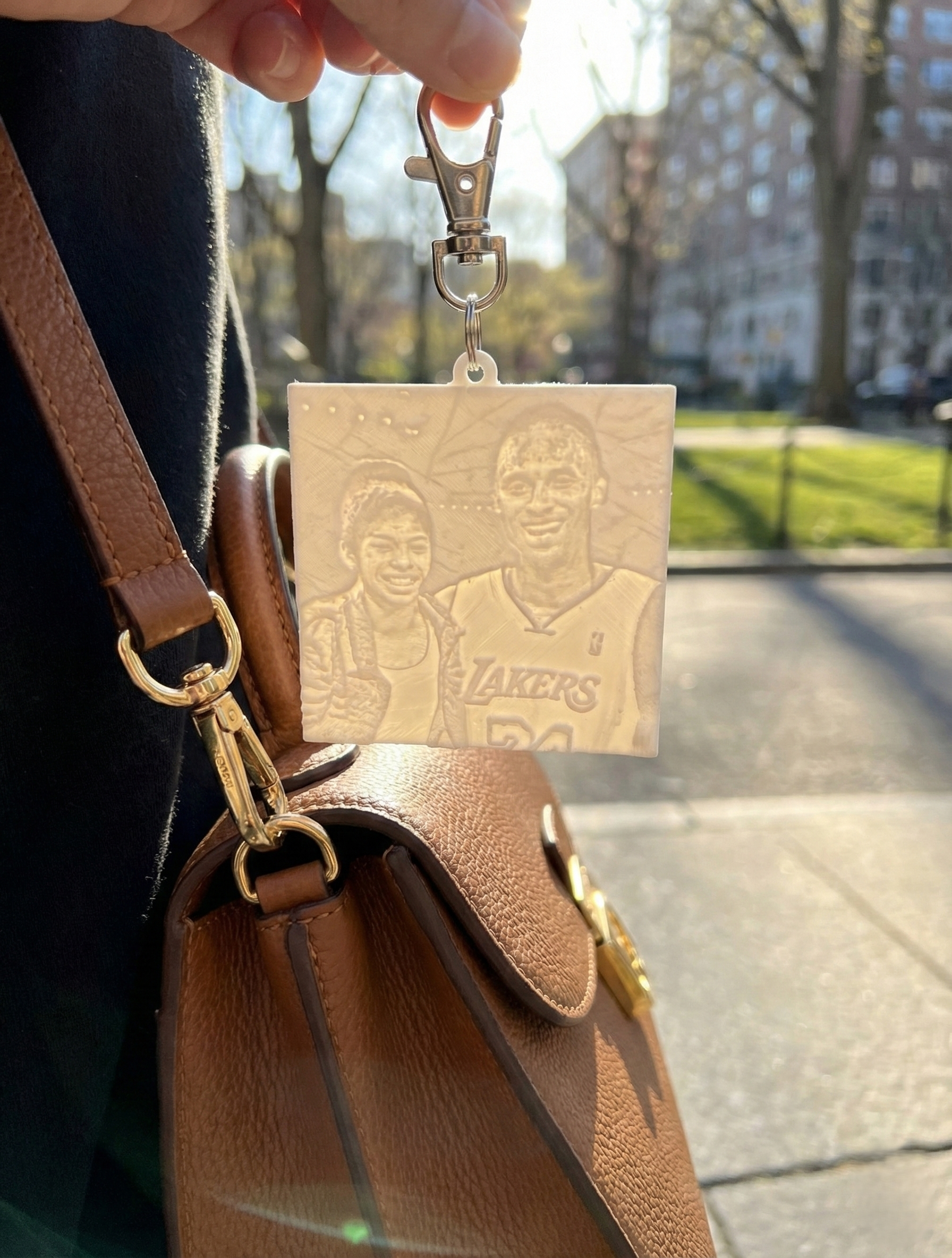 Keychain with etched photo charm hanging from a brown handbag on a sunny sidewalk
