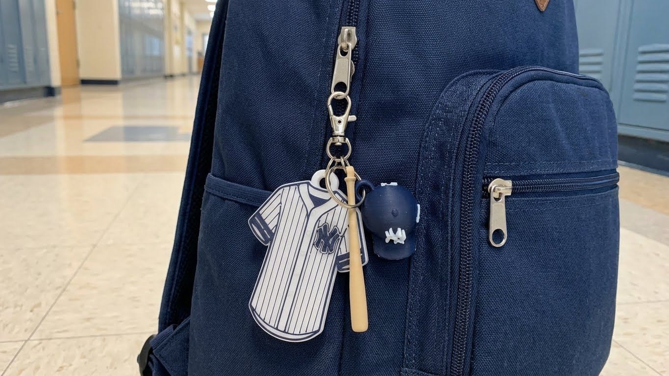 Baseball jersey keychain with ball and bat on a wooden table, with baseballs, gloves, and city skyline in background