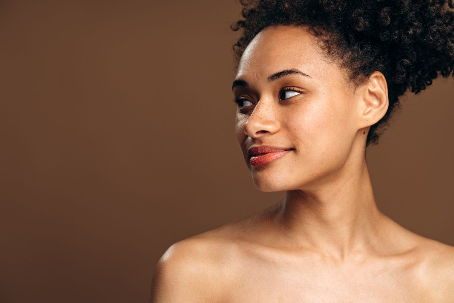 Portrait of a smiling person against a plain brown background, looking to the side