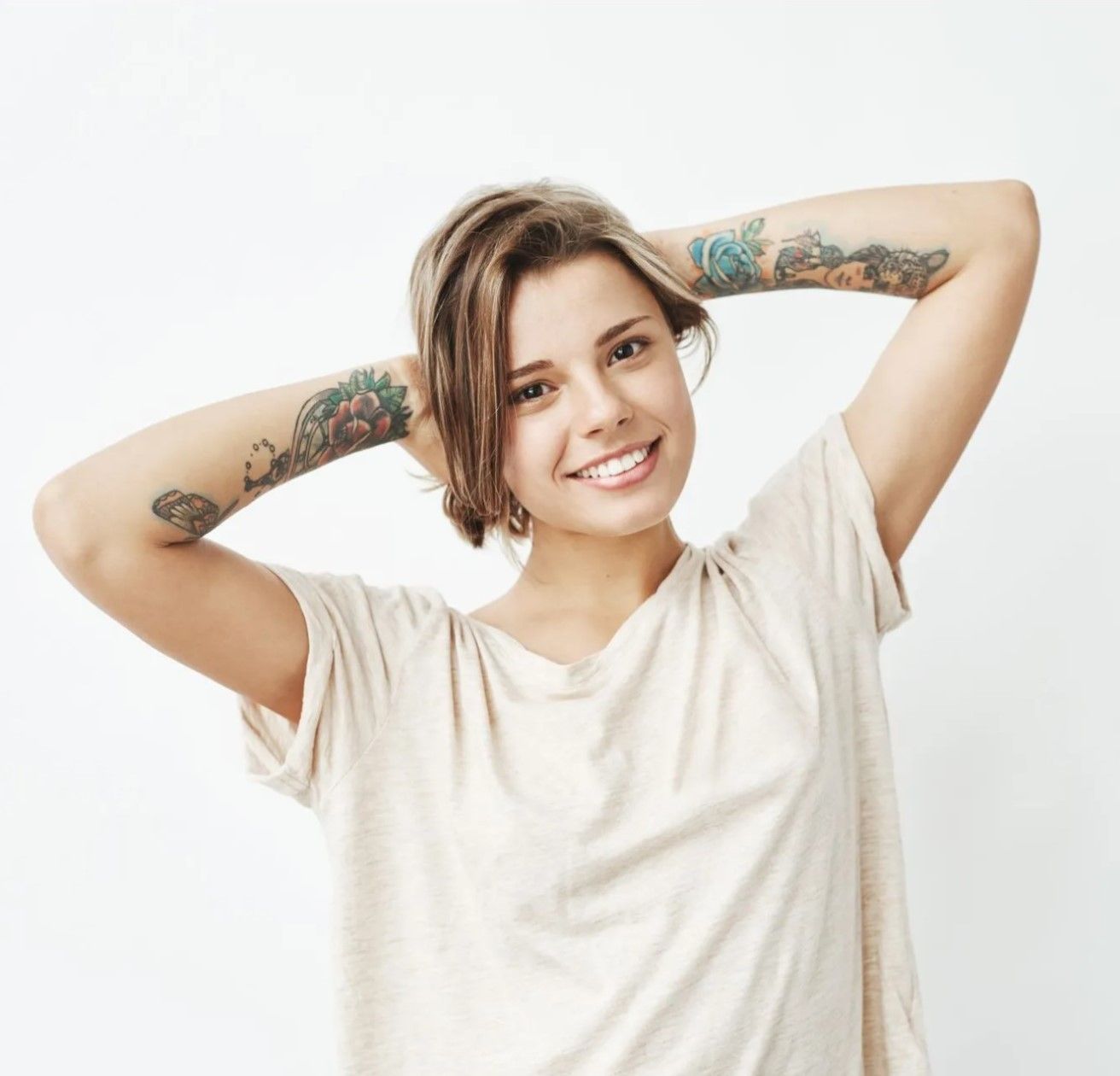 Smiling person with tattooed arms posing against a white background