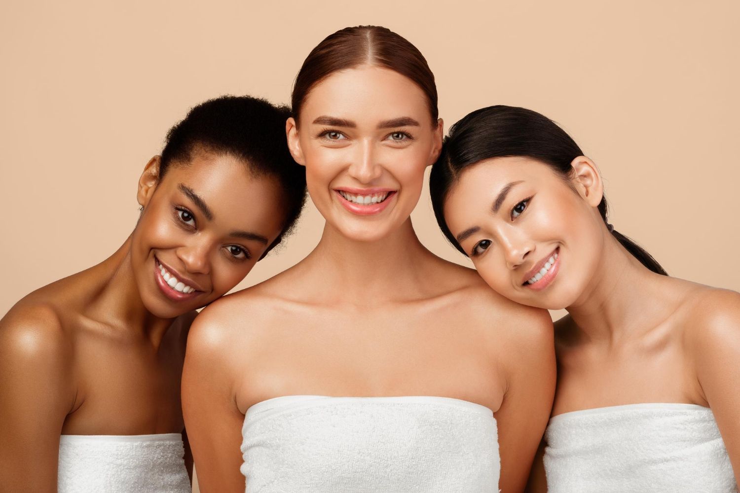 Three smiling people in white towels leaning together against a beige background.