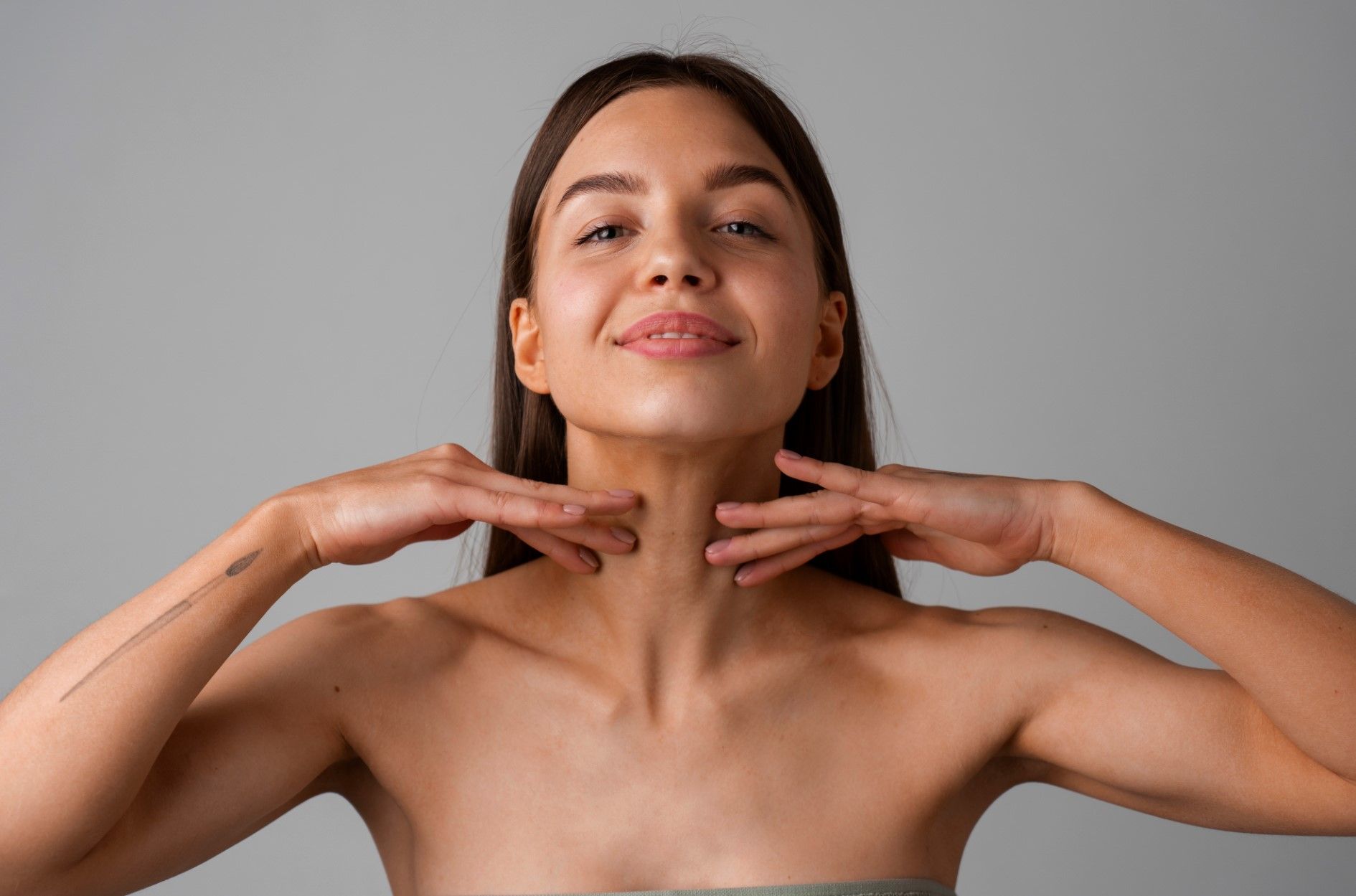 Woman in a black strapless top posing with hands under her chin against a gray background