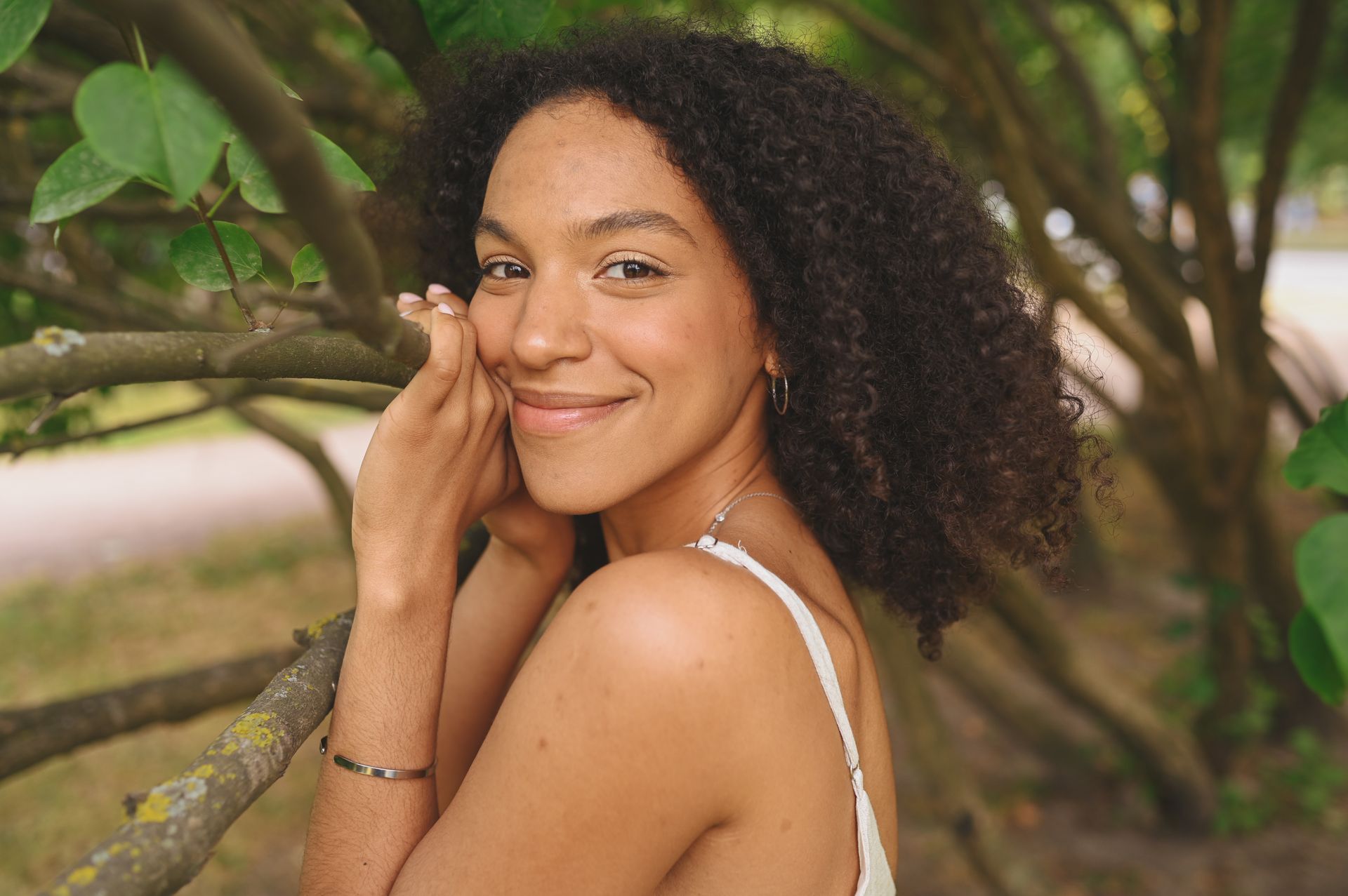 Smiling person leaning against a tree in a green outdoor setting
