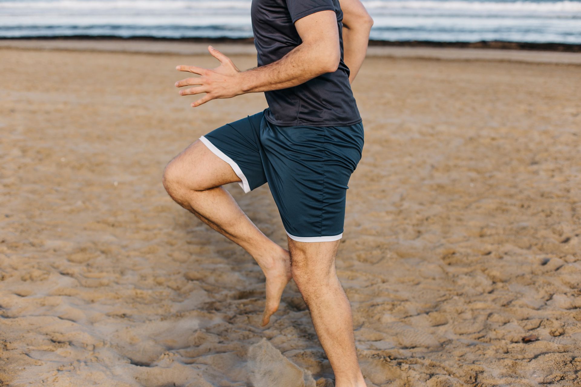 Person stretching on a sandy beach, balancing on one leg near the shoreline
