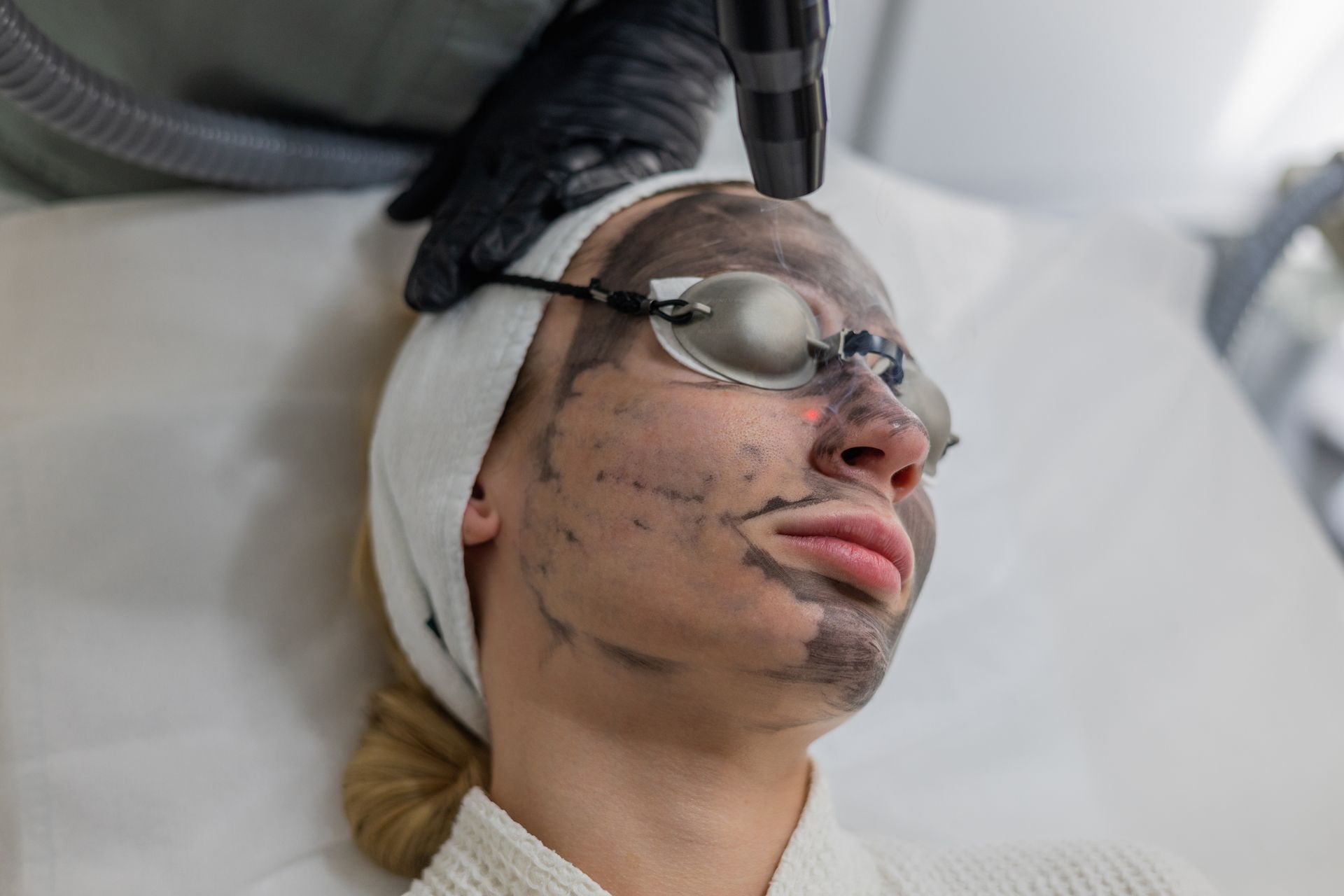 Person receiving a facial treatment with goggles and a head wrap in a spa setting