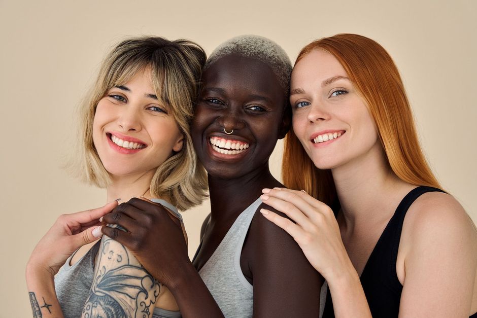 Three smiling women posing closely together against a beige background