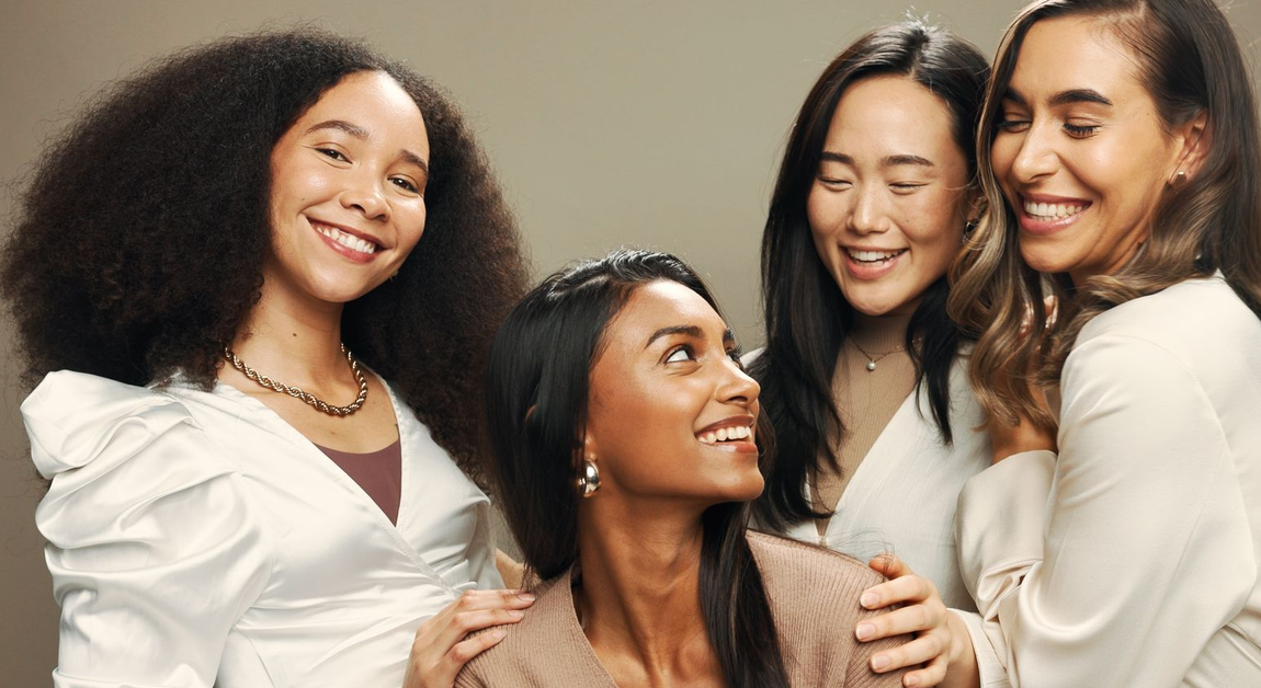 Three smiling friends posing closely together against a light background