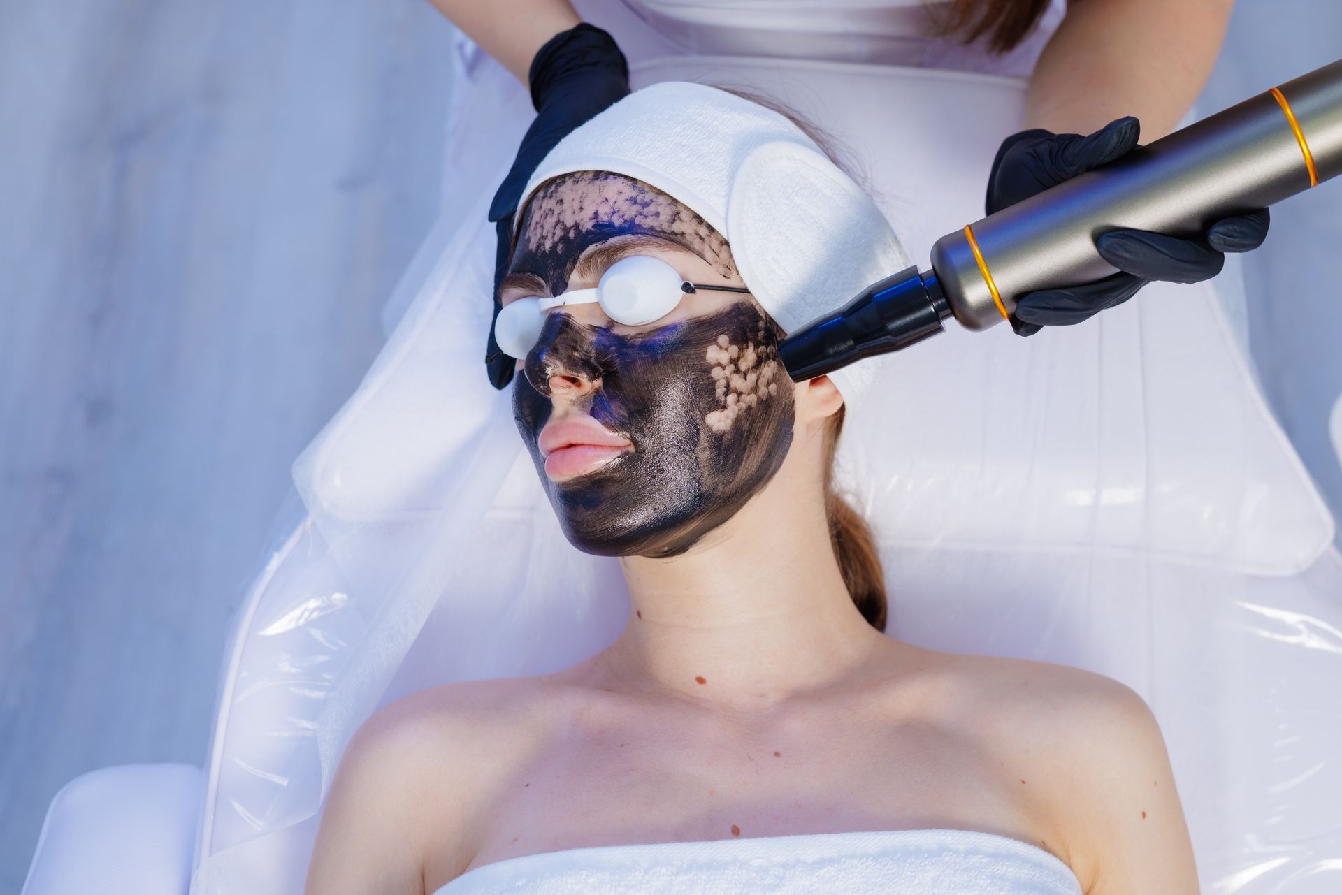 Woman receiving a facial mask treatment with a handheld device while lying on a spa bed