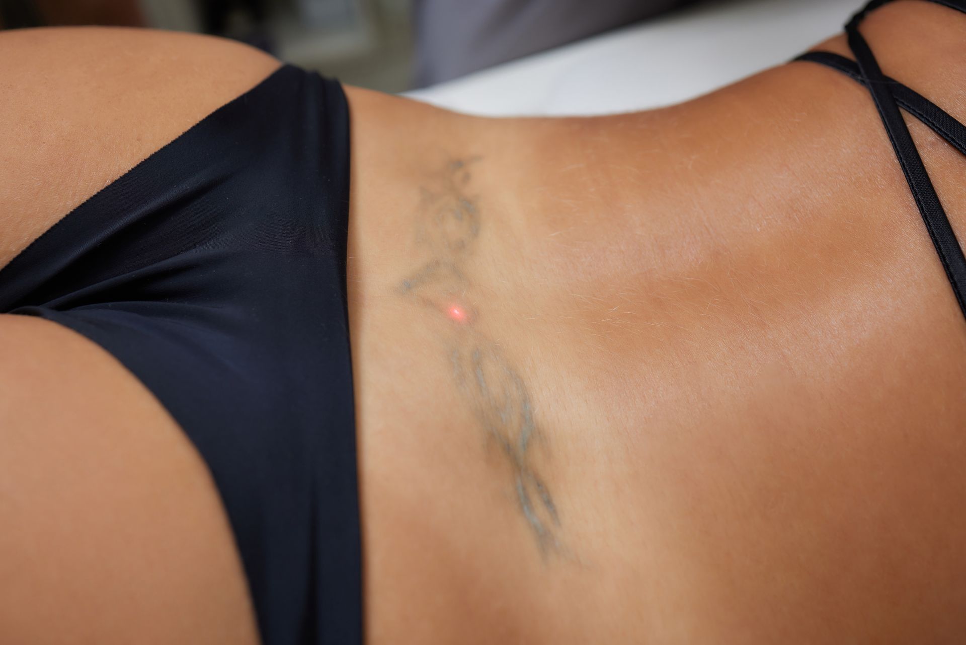 Woman’s torso in a black bikini, showing a faint tattoo on the side.