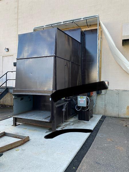 A dark metal dumpster enclosure outside a building, with an open front and electrical panel.