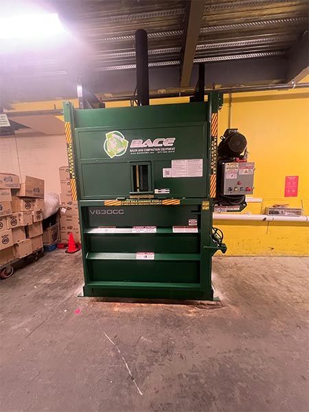 Green industrial cardboard compactor in a warehouse setting.