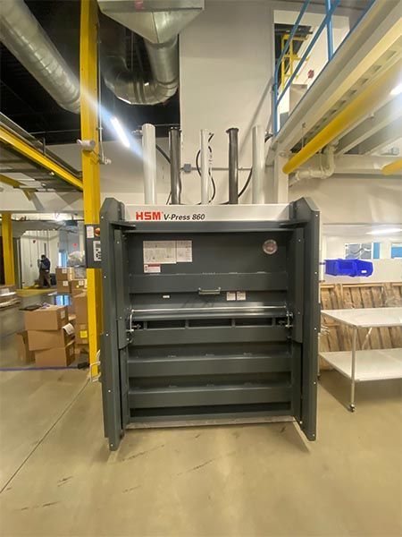 An industrial gray HSM V-Press 260 cardboard baler machine in a warehouse setting.