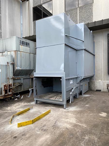 Large gray industrial machinery outside a building, with yellow wheel stops in foreground.
