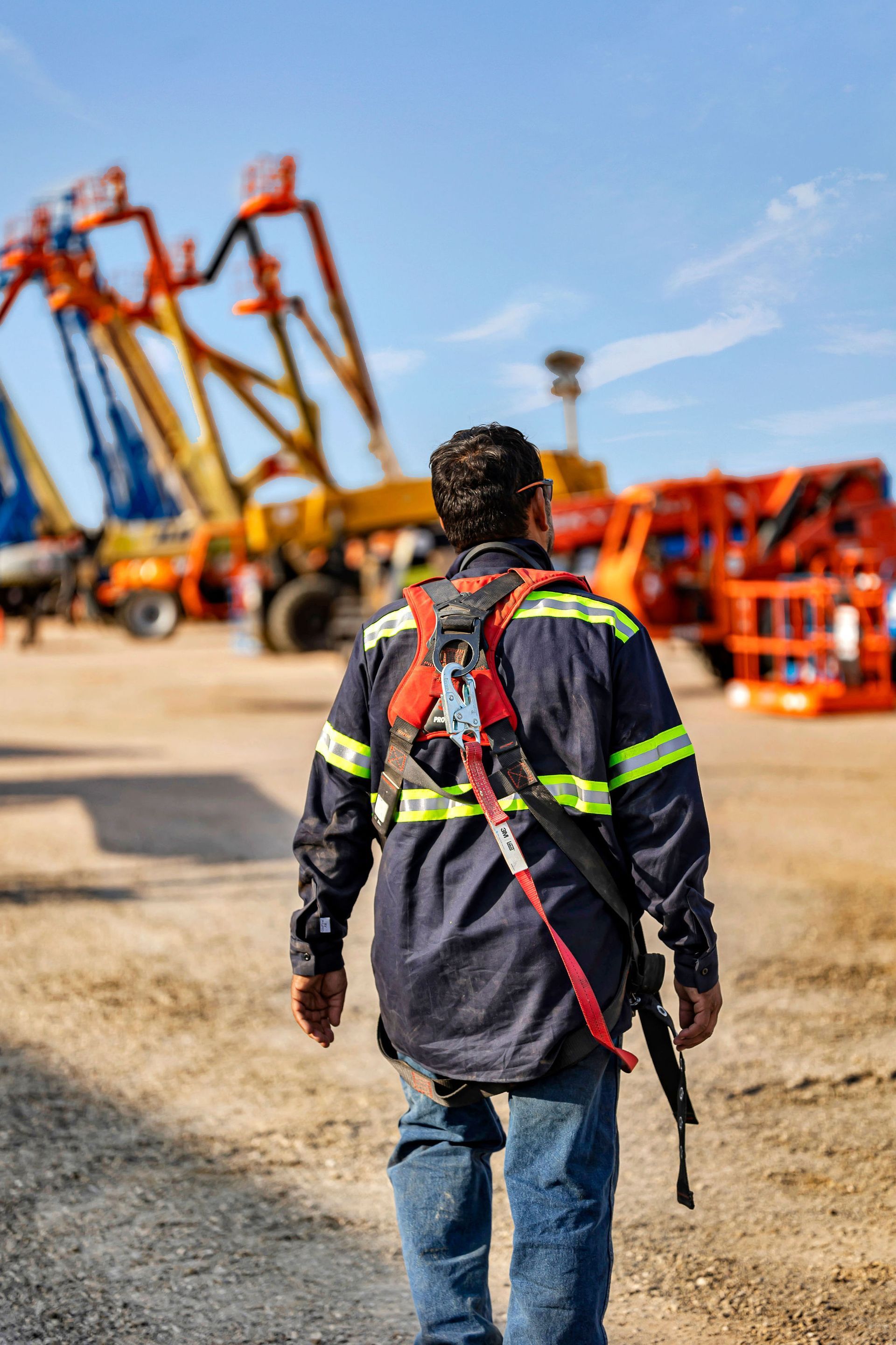 Construction worker in safety gear walks toward machinery in a sunny outdoor work site.