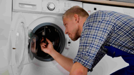 A repairman working on a washing machine, using a screwdriver.