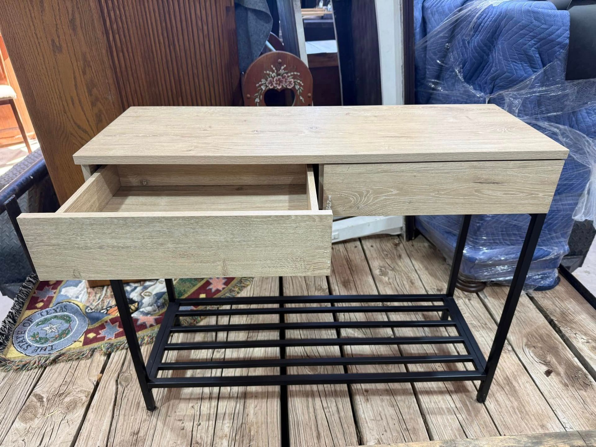 A wooden table with two drawers and a metal shelf on a wooden floor.