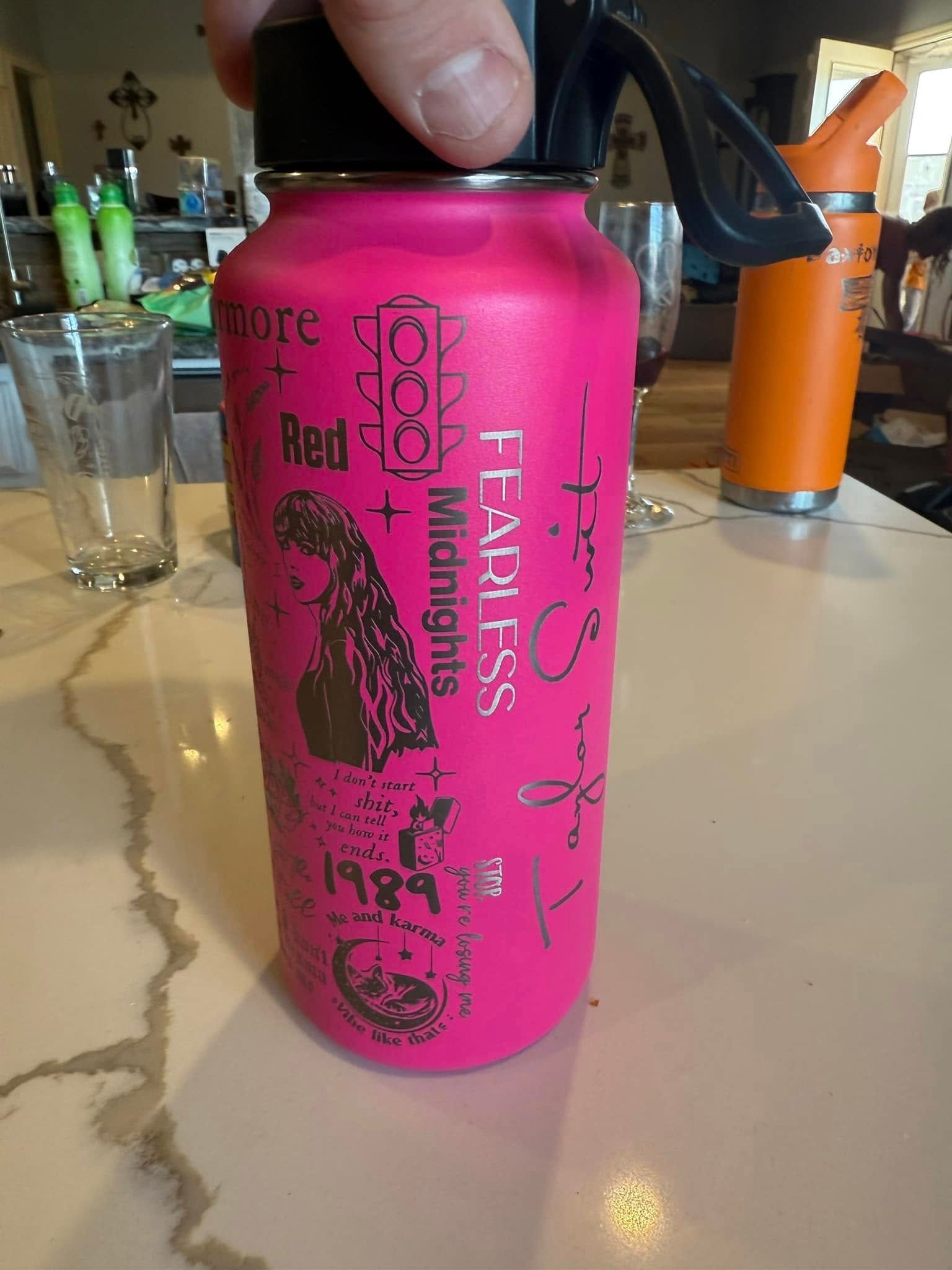 A person is holding a pink water bottle on a table.